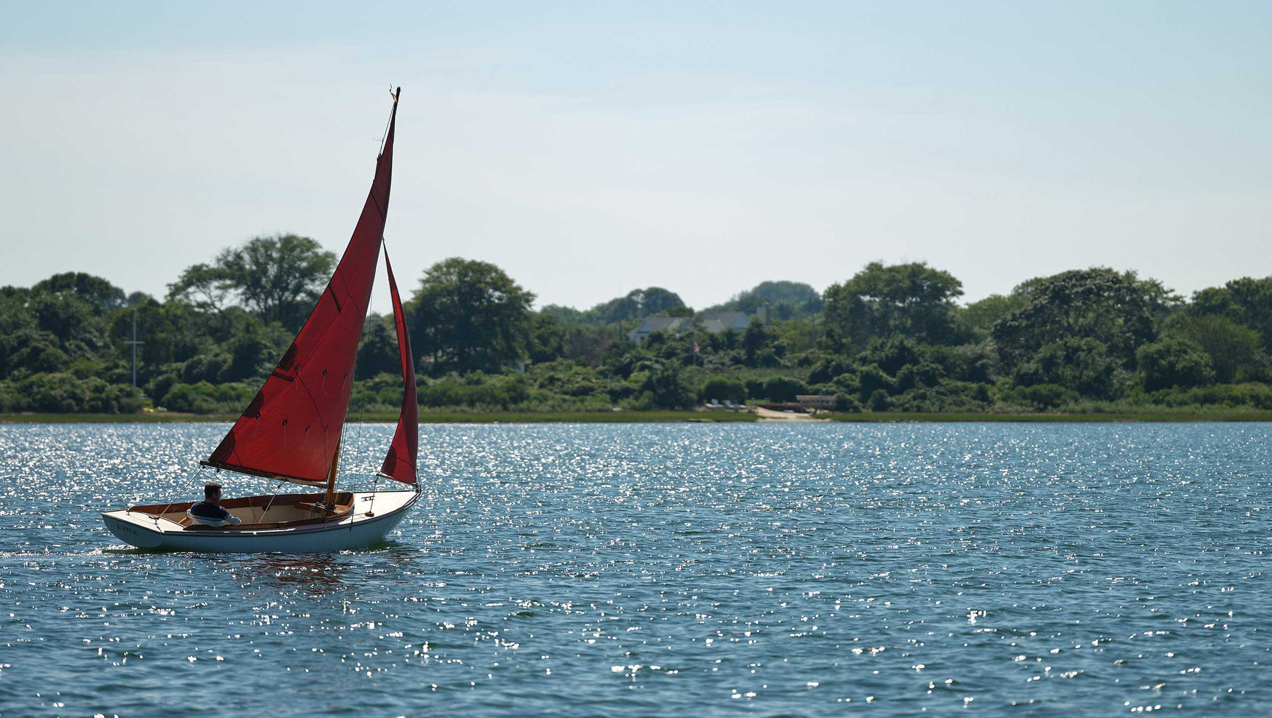 Red and white sail boat on the water with man sitting inside 