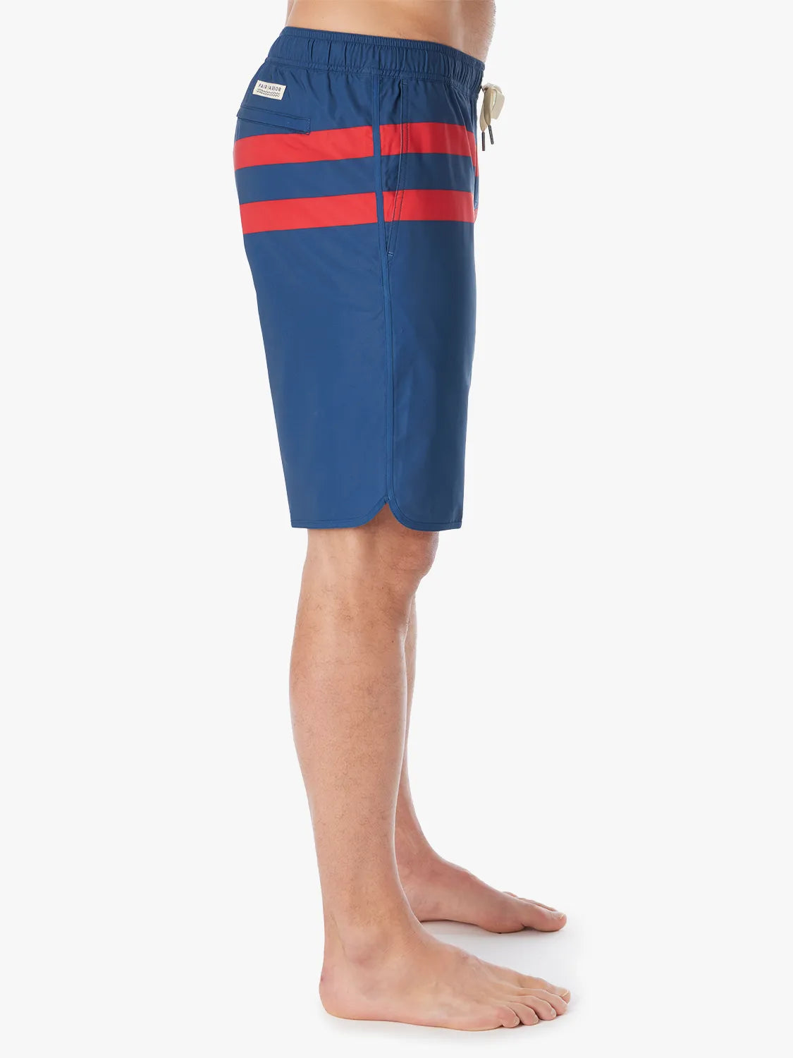 A person wearing a pair of 10 inch navy anchor trunk shorts with two red horizontal stripes and a drawstring waist, showing the side view with a white background.