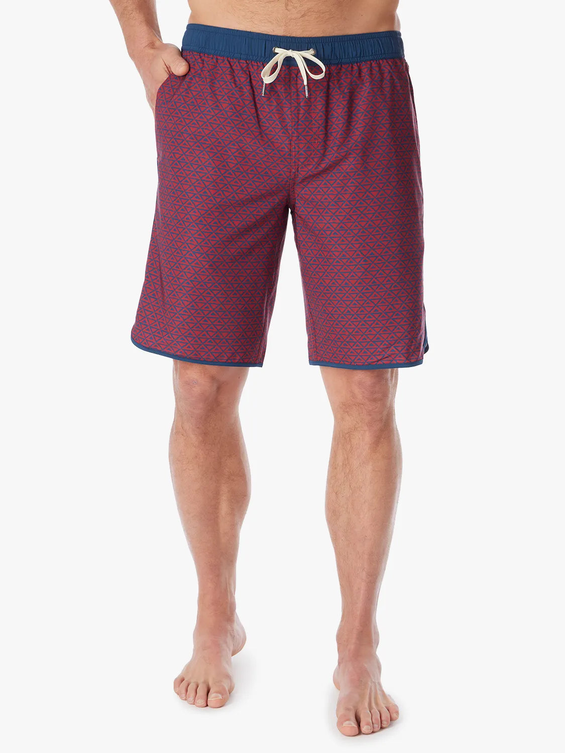 Person wearing a pair of Anchor Trunks with a nautical red wavy geo pattern in 10 Inch inseam. Featuring a drawstring waist and a hand in left side pocket, with a white background.