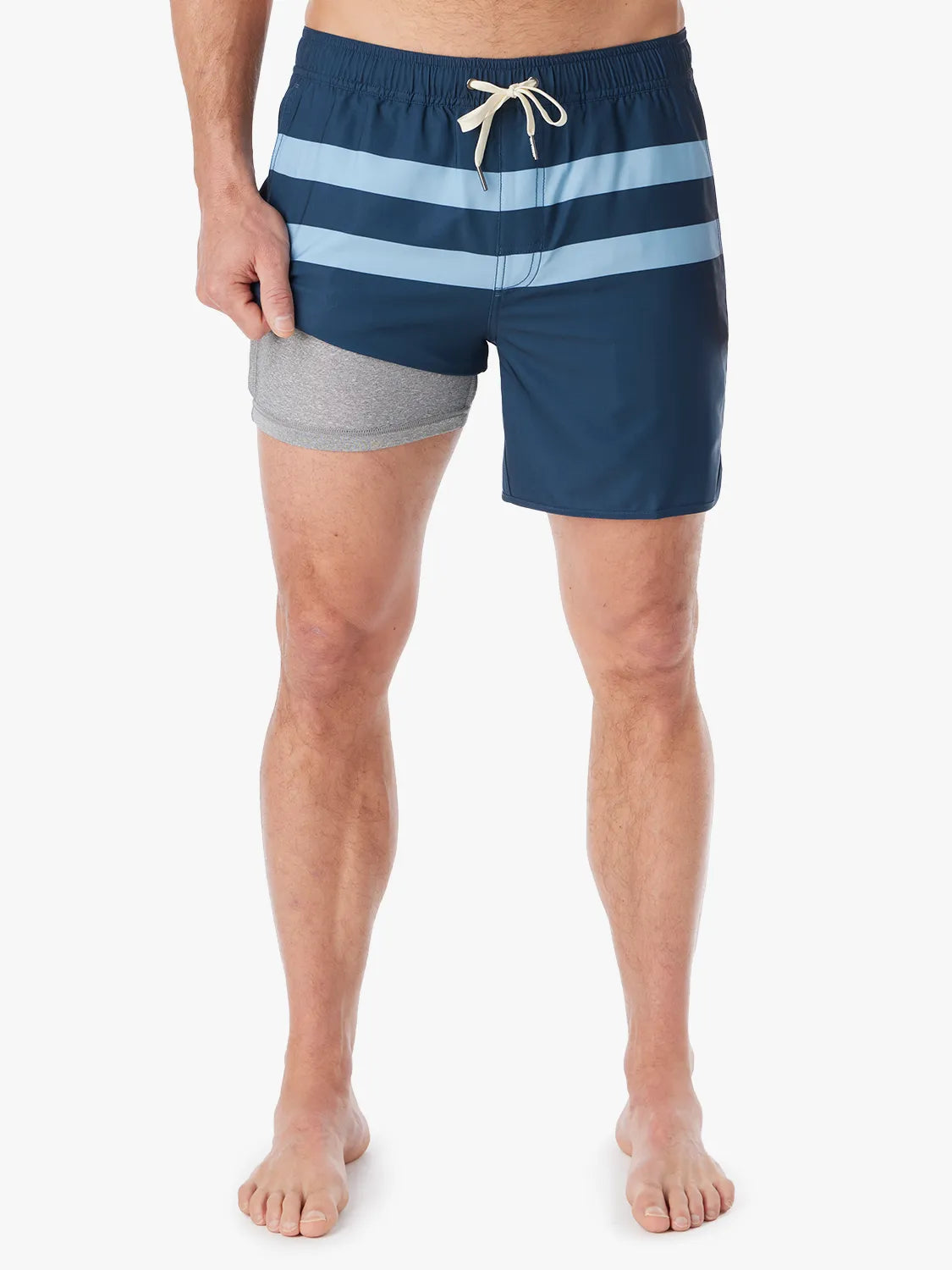 A person wearing a pair of 6 inch navy anchor trunk shorts with two light blue horizontal stripes and a drawstring waist, showing the liner with a white background.
