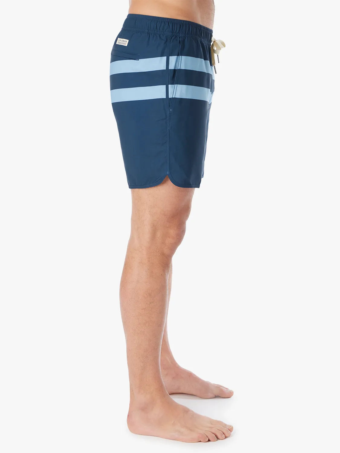 A person wearing a pair of 6 inch navy anchor trunk shorts with two light blue horizontal stripes and a drawstring waist, showing the side view with a white background.