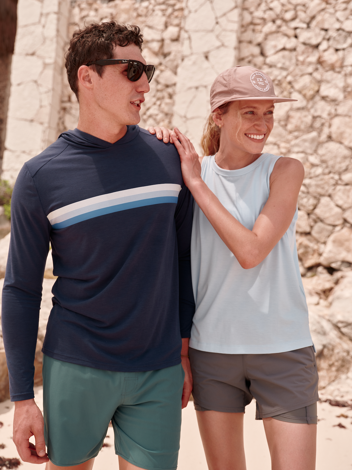 A couple standing side by side, the man on the left wearing Anchor trunk in seapine and seabreeze hoodie in ombre stripe.