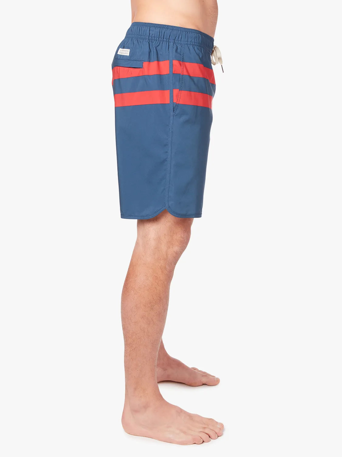 A person wearing a pair of 8 inch navy anchor trunk shorts with two red horizontal stripes and a drawstring waist, showing the side view with a white background.