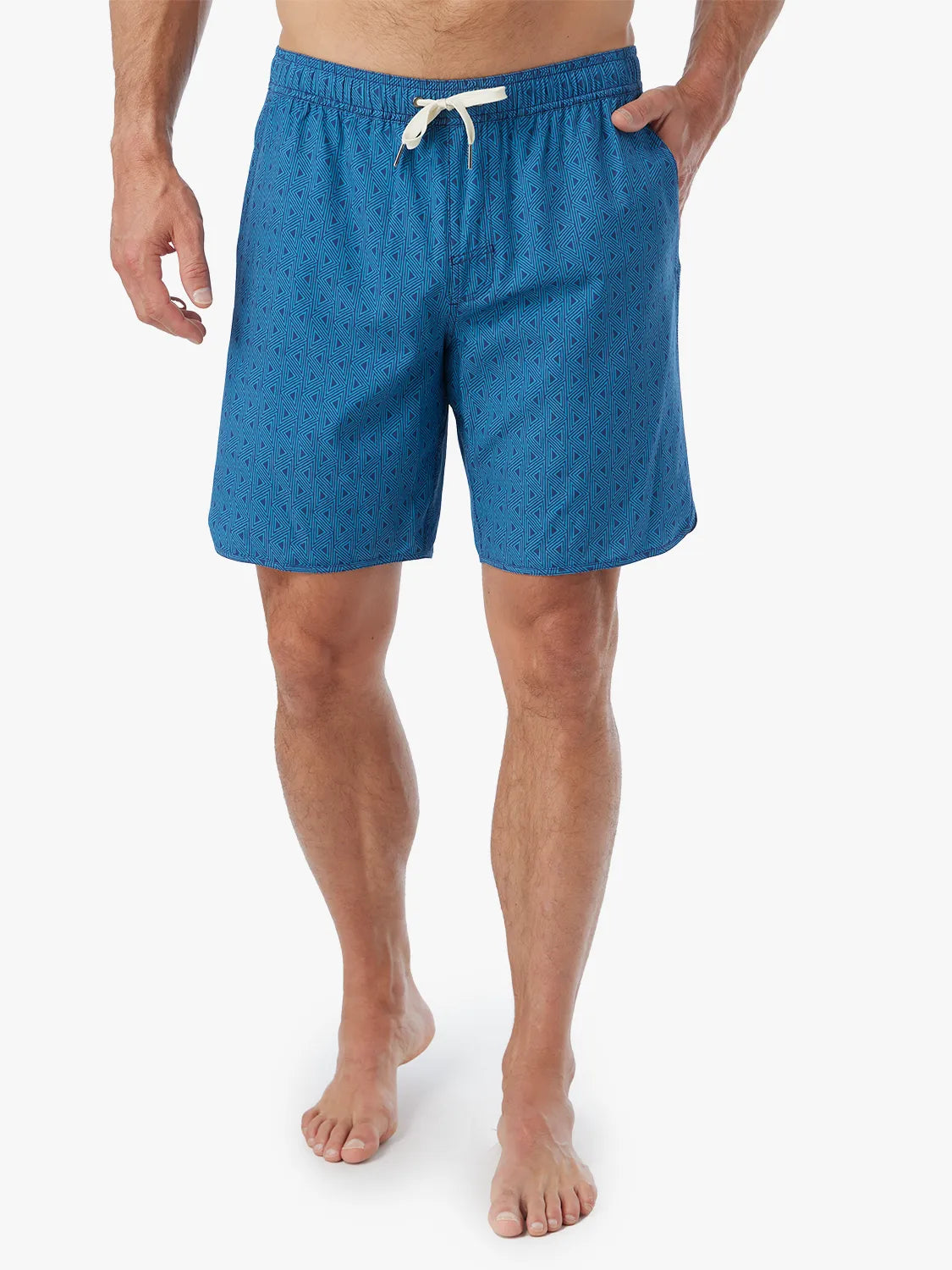 Person wearing electric blue geometric patterned Anchor Trunk in 8 inch inseam with a drawstring waistband and hand in side pocket.