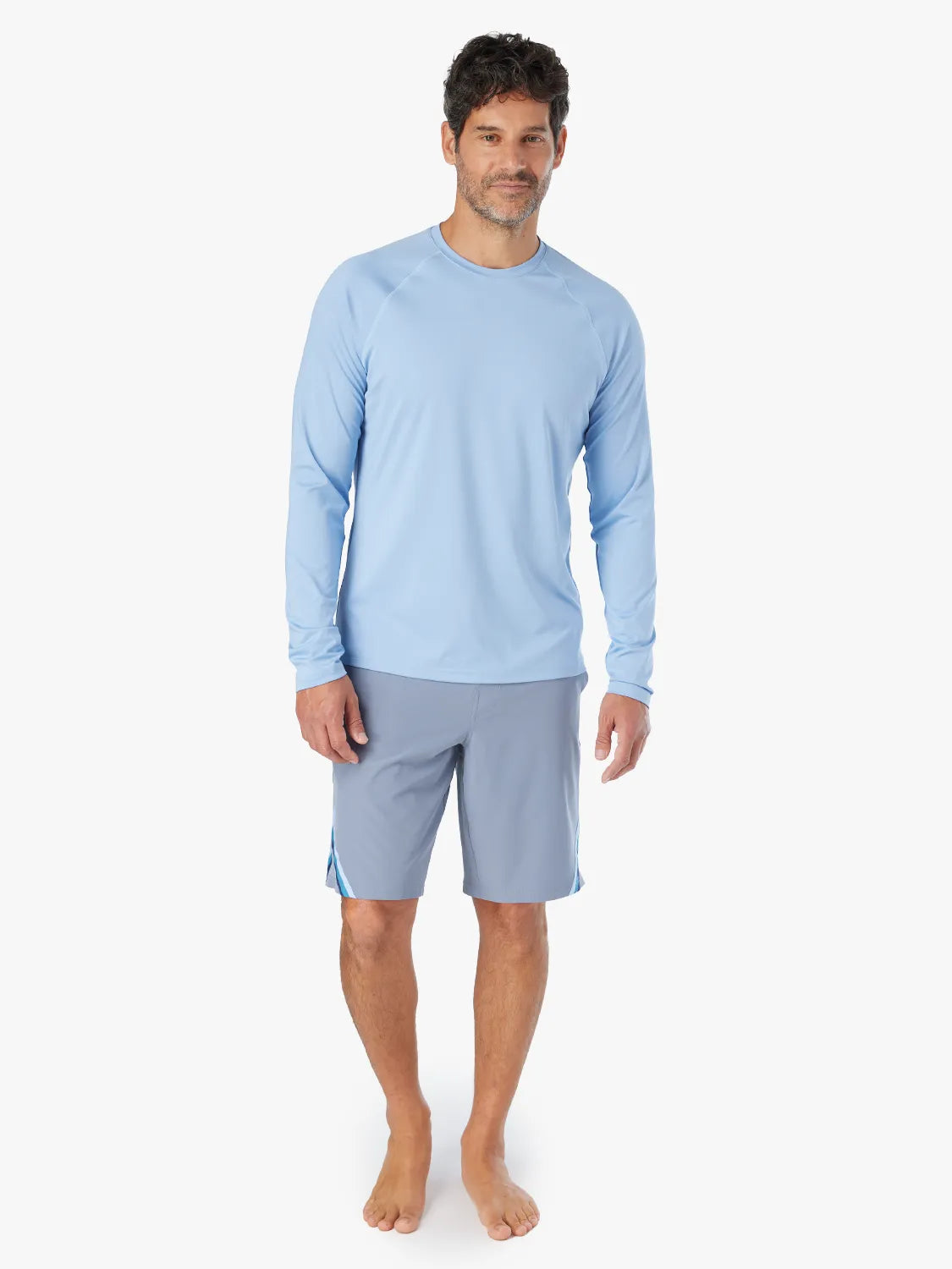 A person wearing the long-sleeved light blue Anchor Rashguard with a crewneck design, showing full body view. Paired with Ozone Board Short.