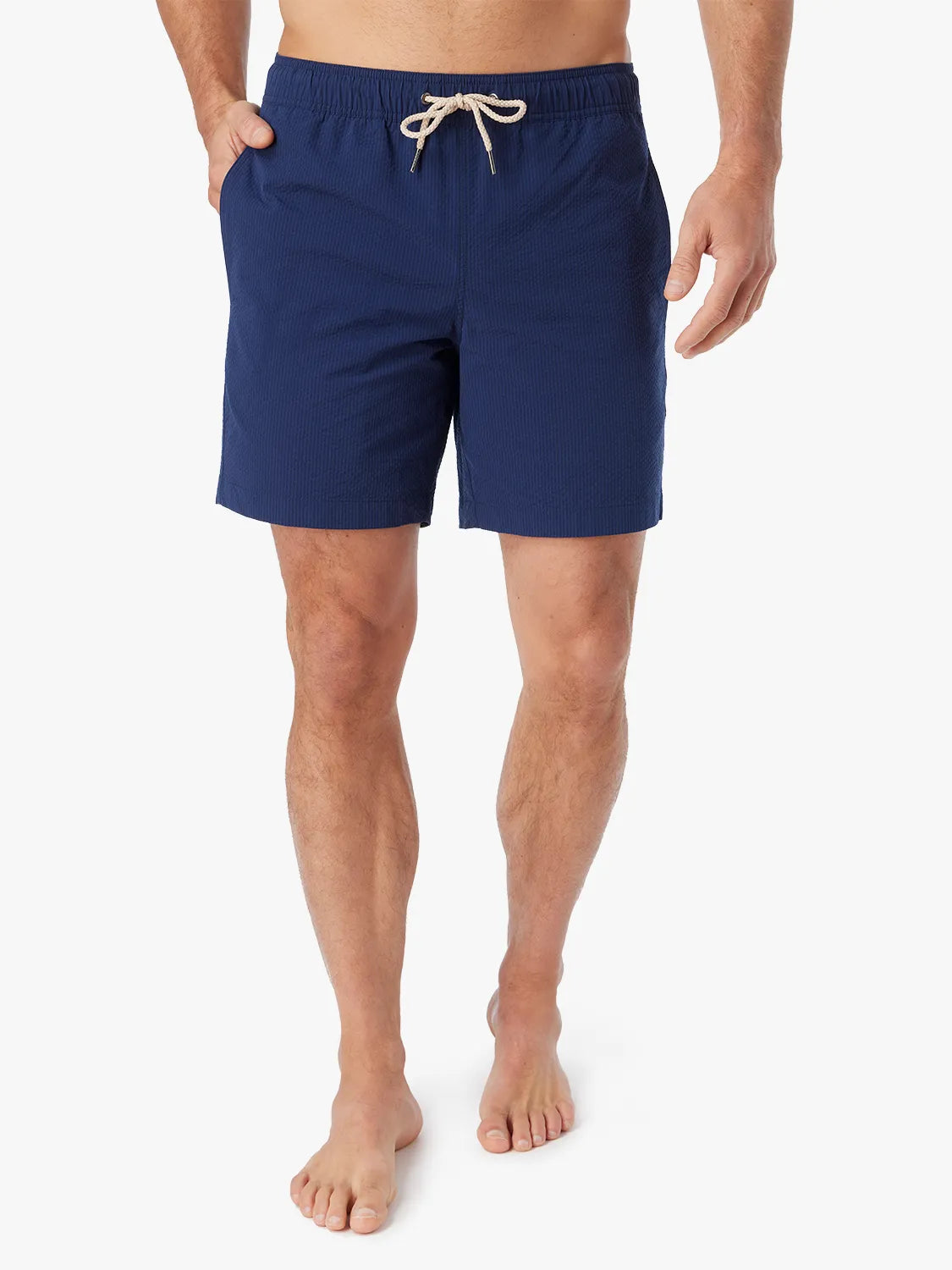 Person wearing a pair Bayberry swim trunks in Navy blue seersucker with a drawstring waistband and hand in side pocket.