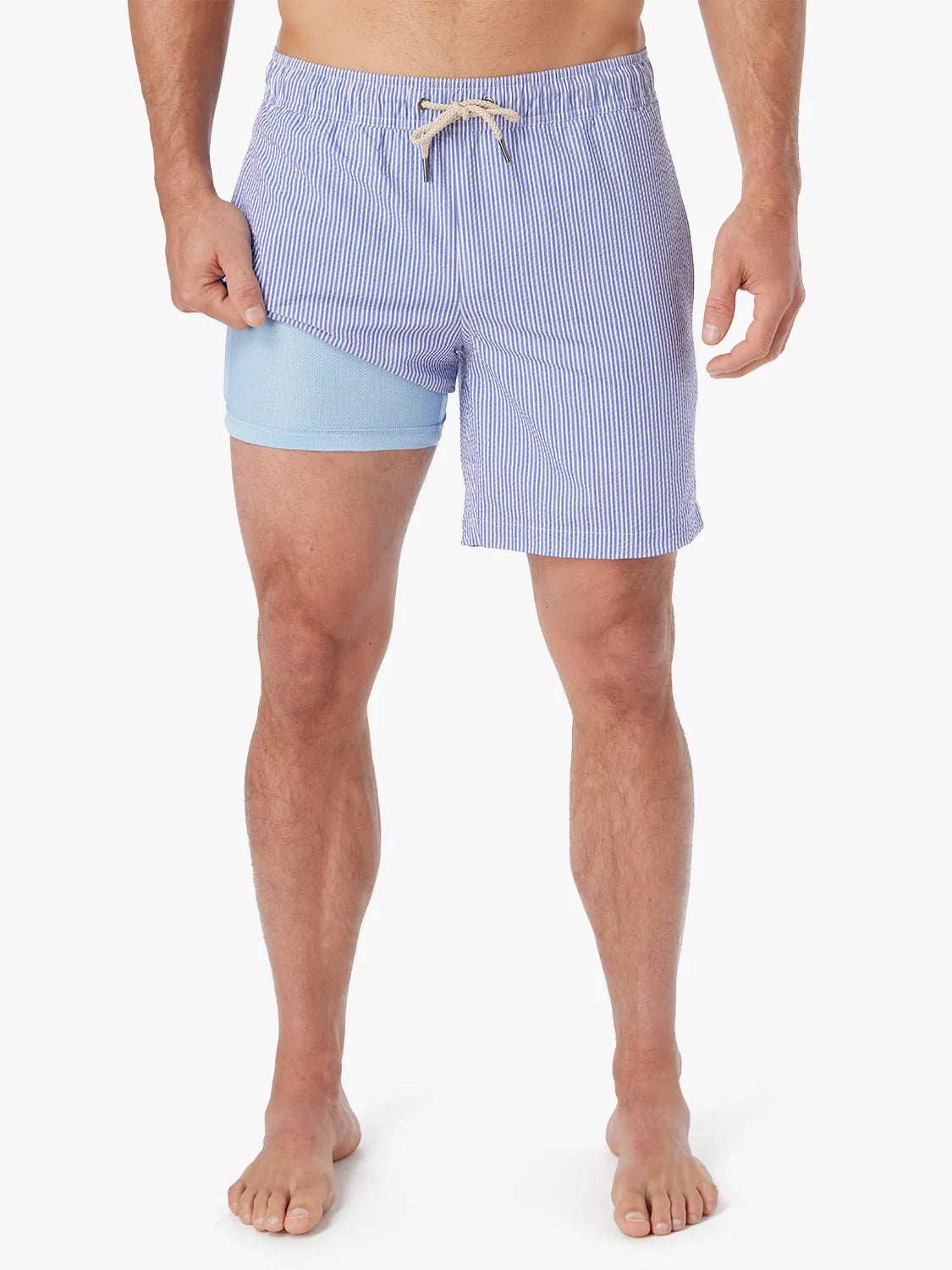 Man wearing a pair of light blue seersucker Bayberry swim trunks with a drawstring elastic waistband, showing the liner.