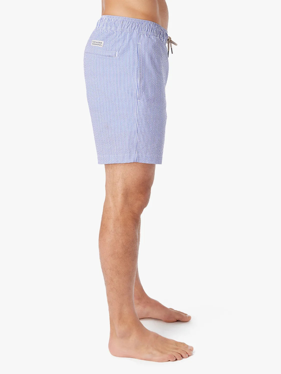 Man wearing a pair of light blue seersucker Bayberry swim trunks with a drawstring elastic waistband, showing the side view.