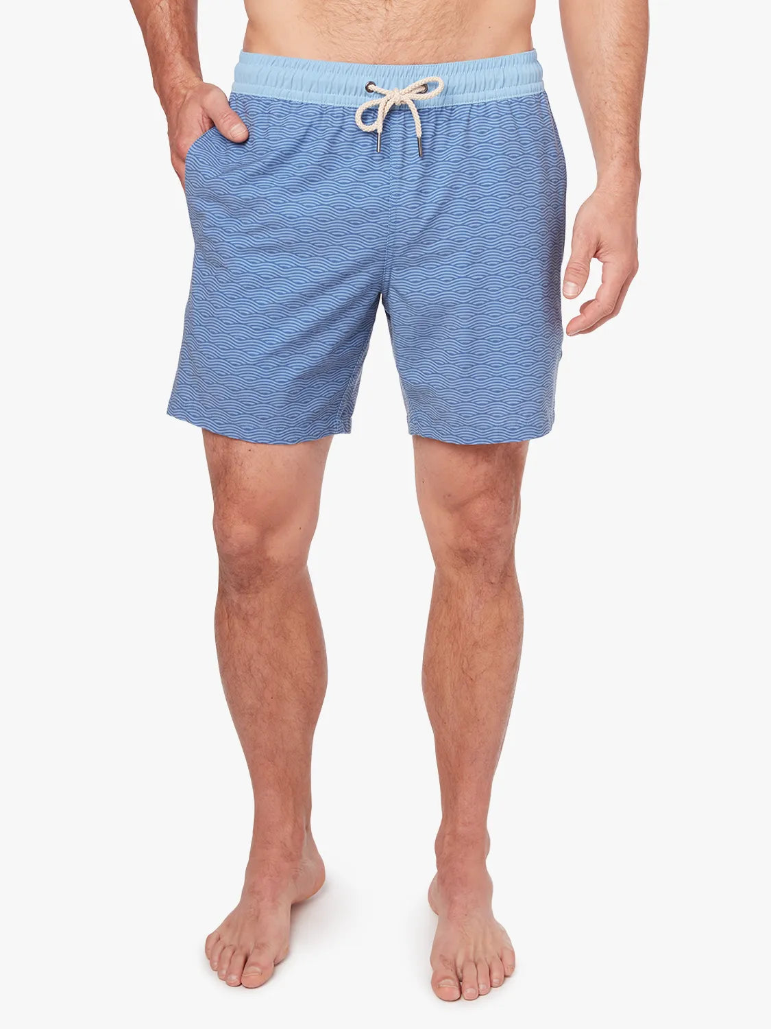 A person wearing a pair of blue waves Bayberry trunks with a drawstring elastic waistband, having a hand in side pocket.