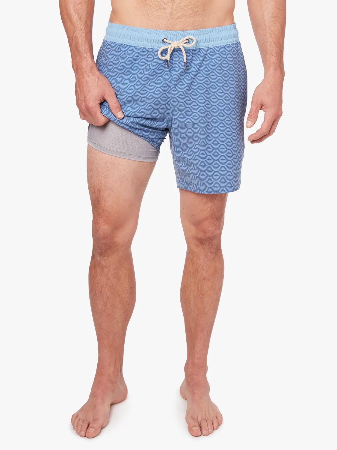 A person wearing a pair of blue waves Bayberry trunks with a drawstring elastic waistband, showing the liner.