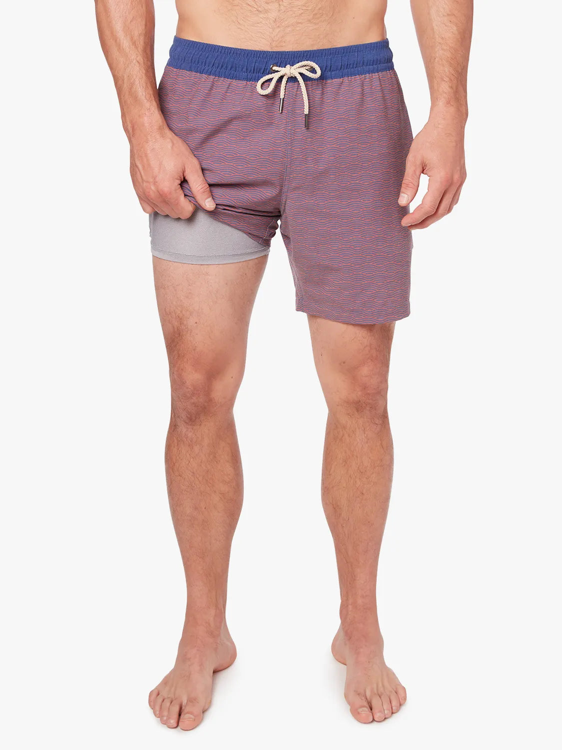 Person wearing a pair of red bayberry trunks with a navy waistband and subtle wave pattern with a white drawstring on a white background. Showing the liner underneath.