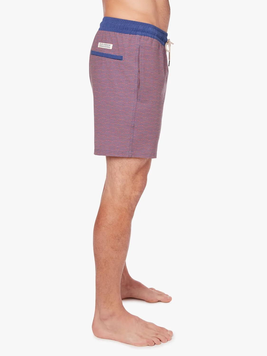 Person wearing a pair of red bayberry trunks with a navy waistband and subtle wave pattern with a white drawstring on a white background. Showing the side view.