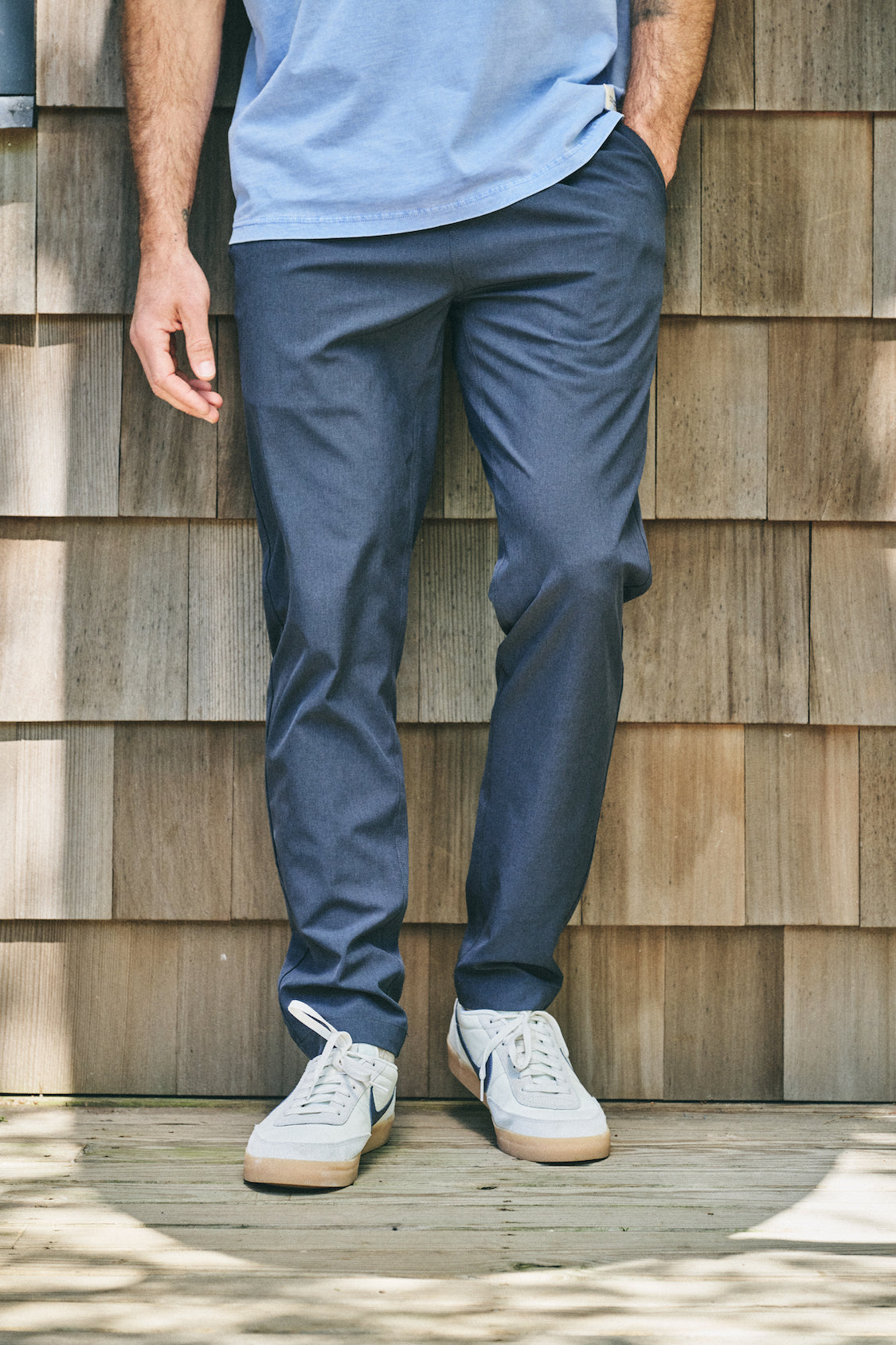 Person wearing a pair of navy blue one pants while standing on outside deck, paired with tshirt and white sneakers.