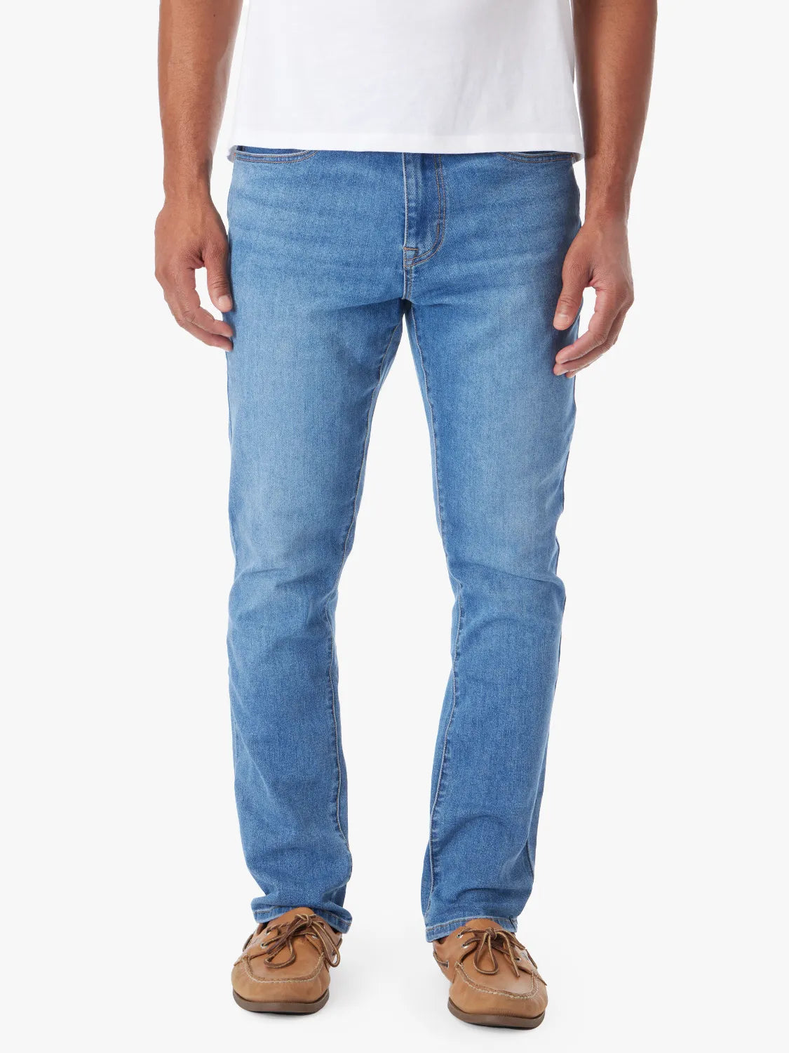 Person wearing a pair of men's straight-fit blue denim jeans with a 5-pocket design on a white background. Paired with white tee and boat shoes.