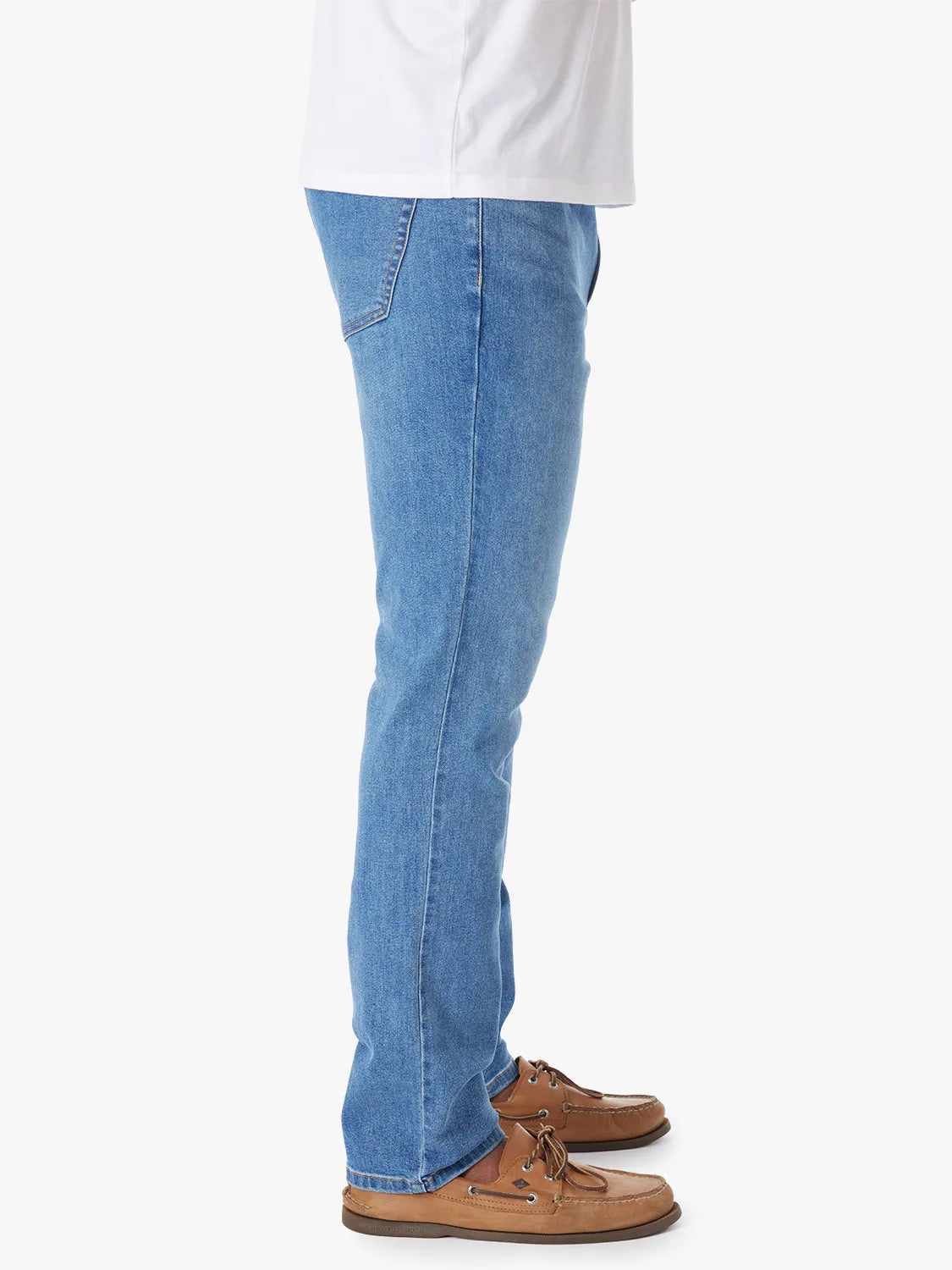 Person wearing a pair of men's straight-fit blue denim jeans with a 5-pocket design on a white background. Paired with white tee and boat shoes, showing the side view.