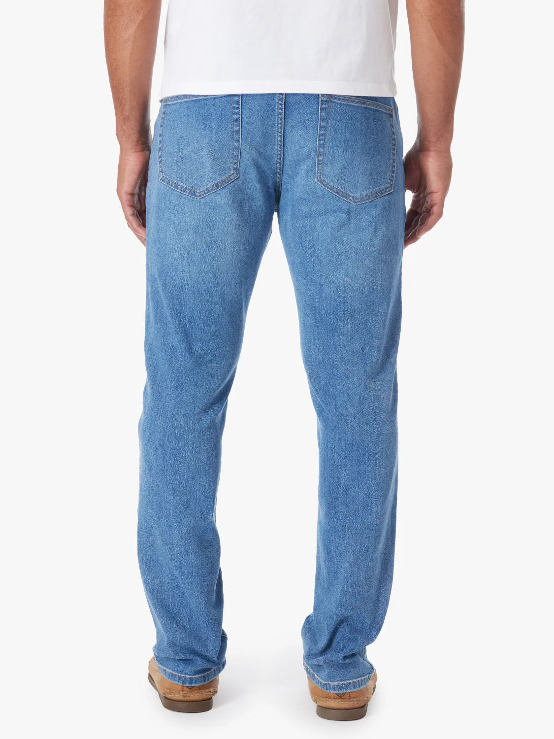 Person wearing a pair of men's straight-fit blue denim jeans with a 5-pocket design on a white background. Paired with white tee and boat shoes, showing the back view.