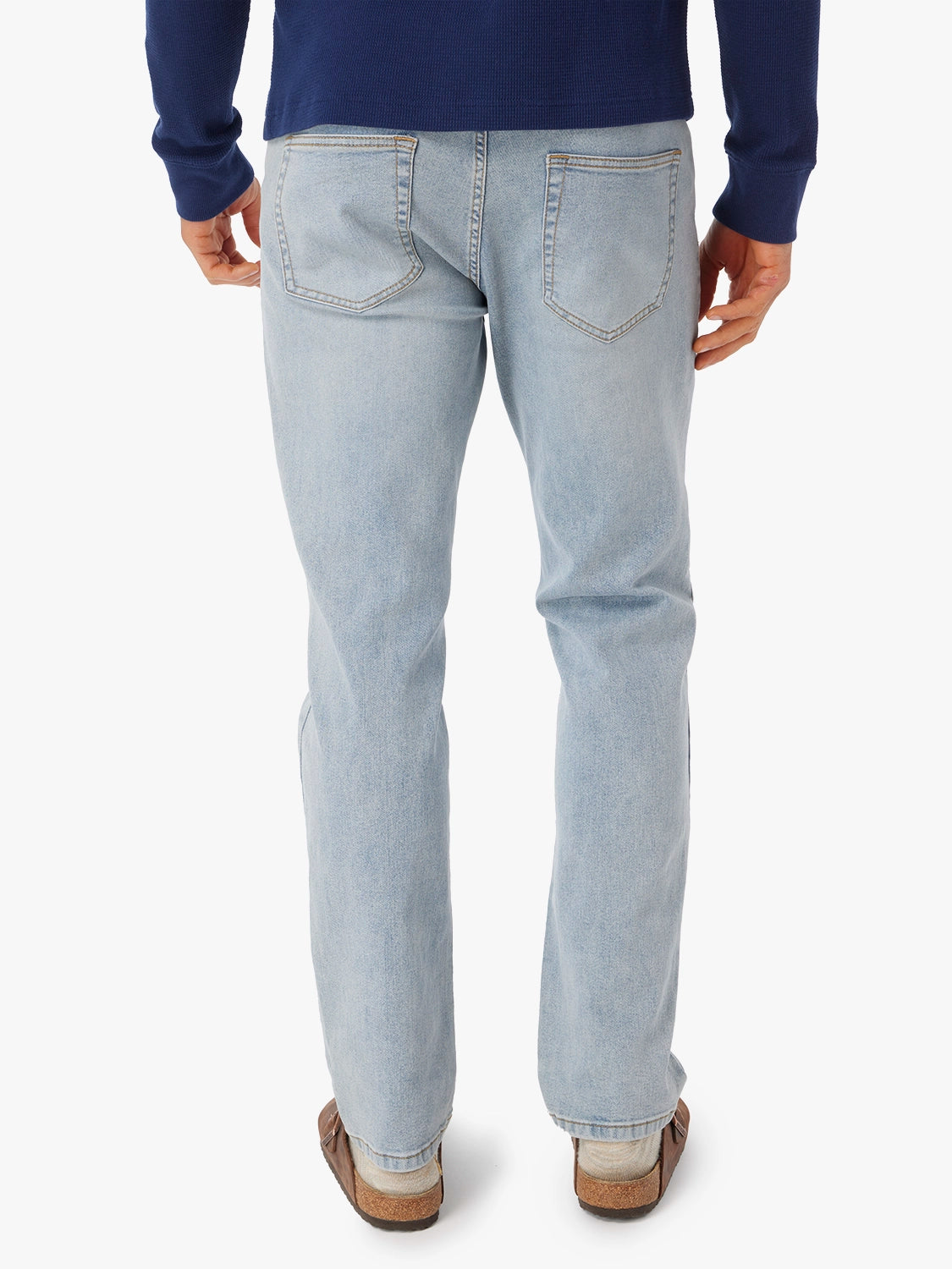 Person wearing a pair of light wash driftwood jeans, showing the back view on a white background