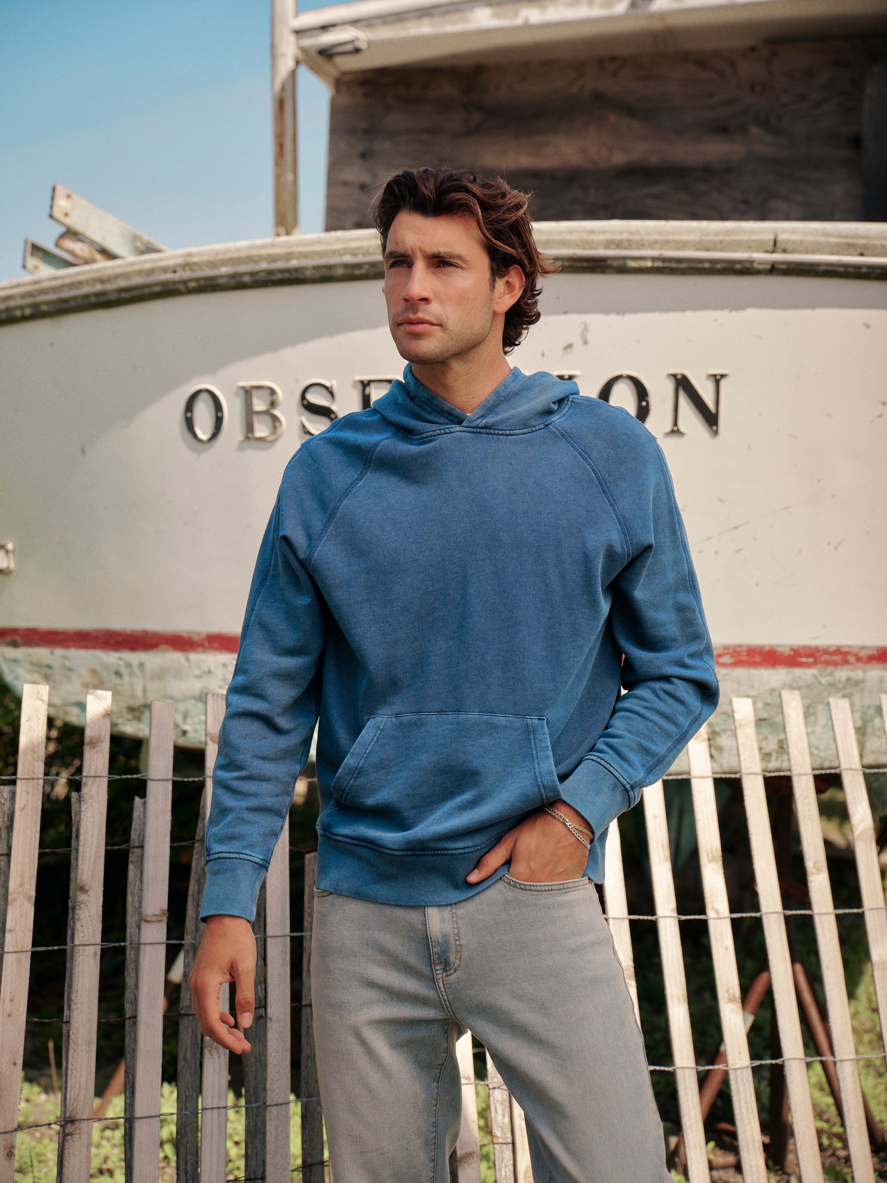 Man wearing a navy blue saltaire hoodie standing in front of docked boat.