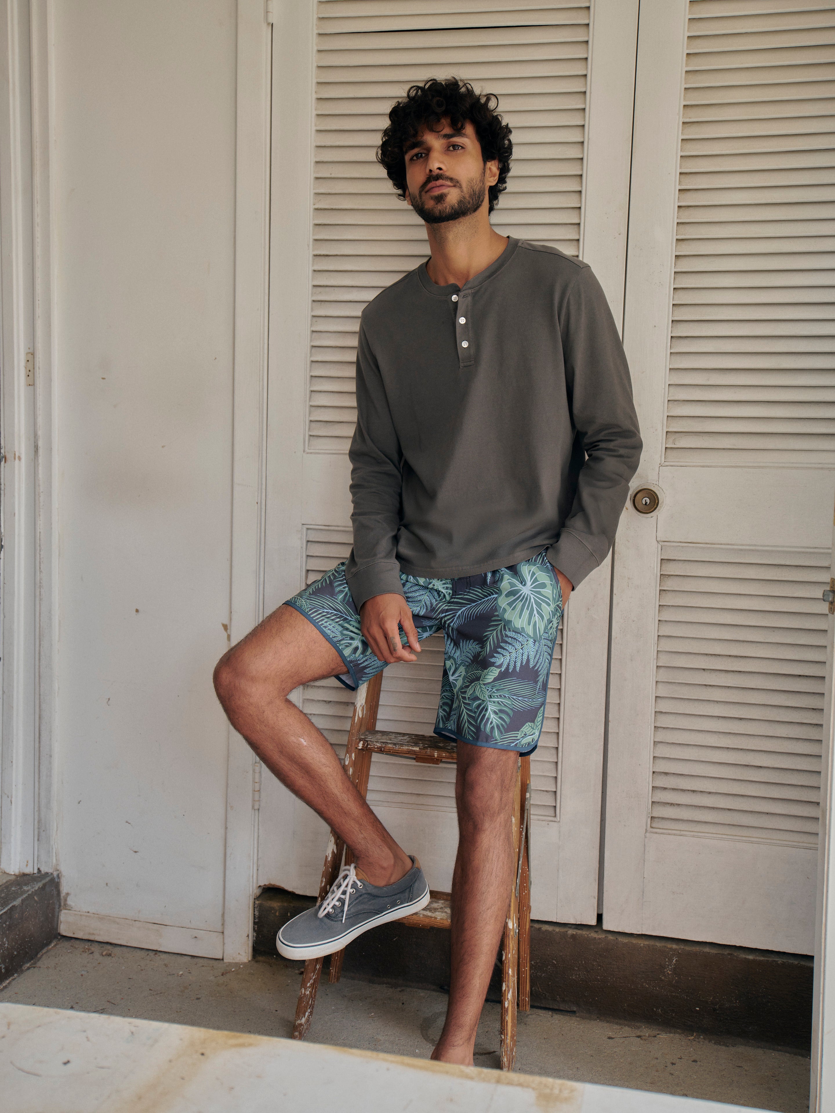 Man wearing a black long-sleeve henley shirt and patterned anchor trunks sitting on a chair.