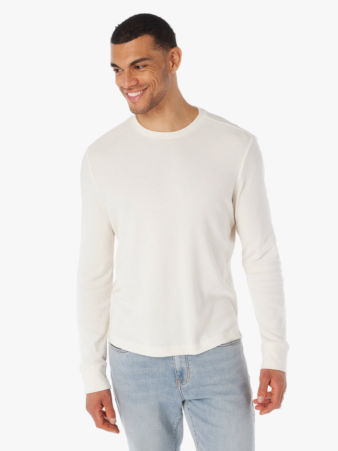 Man wearing beige hudson waffle crewneck long sleeve shirt on a white background, paired with driftwood denim pants.