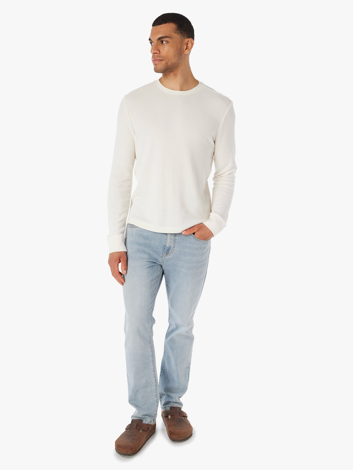 Man wearing beige hudson waffle crewneck long sleeve shirt on a white background, paired with driftwood denim pants.
