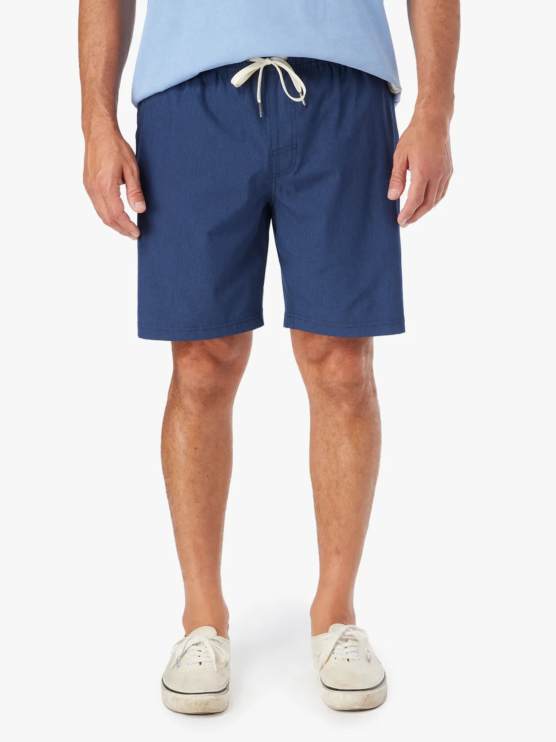 Person wearing a pair of blue 8 inch one shorts with a drawstring on a white background. Paired with a tshirt and white sneakers.