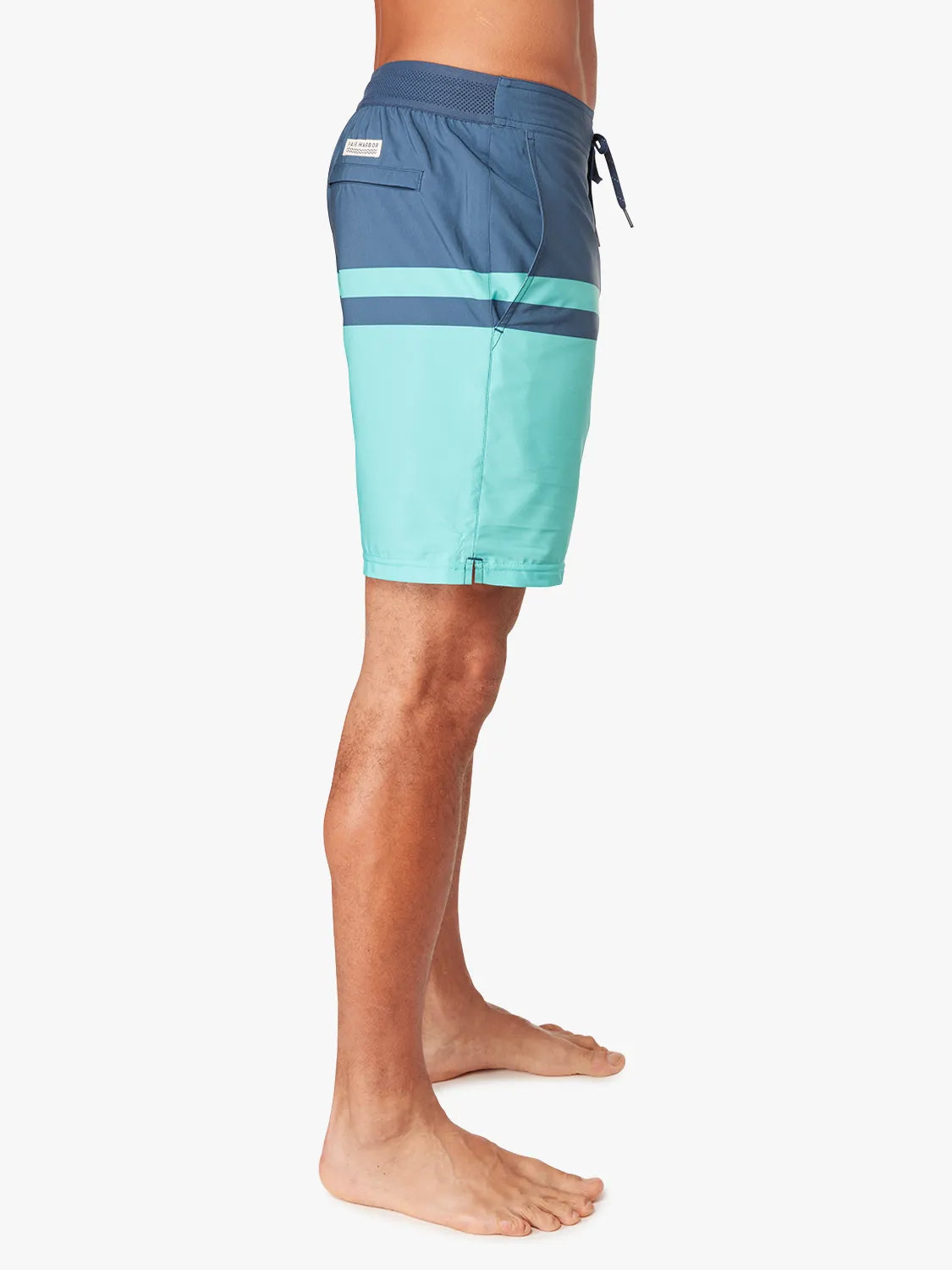 Person wearing a pair of navy blue and teal color blocked ozone board shorts on a white background, showing the side view.