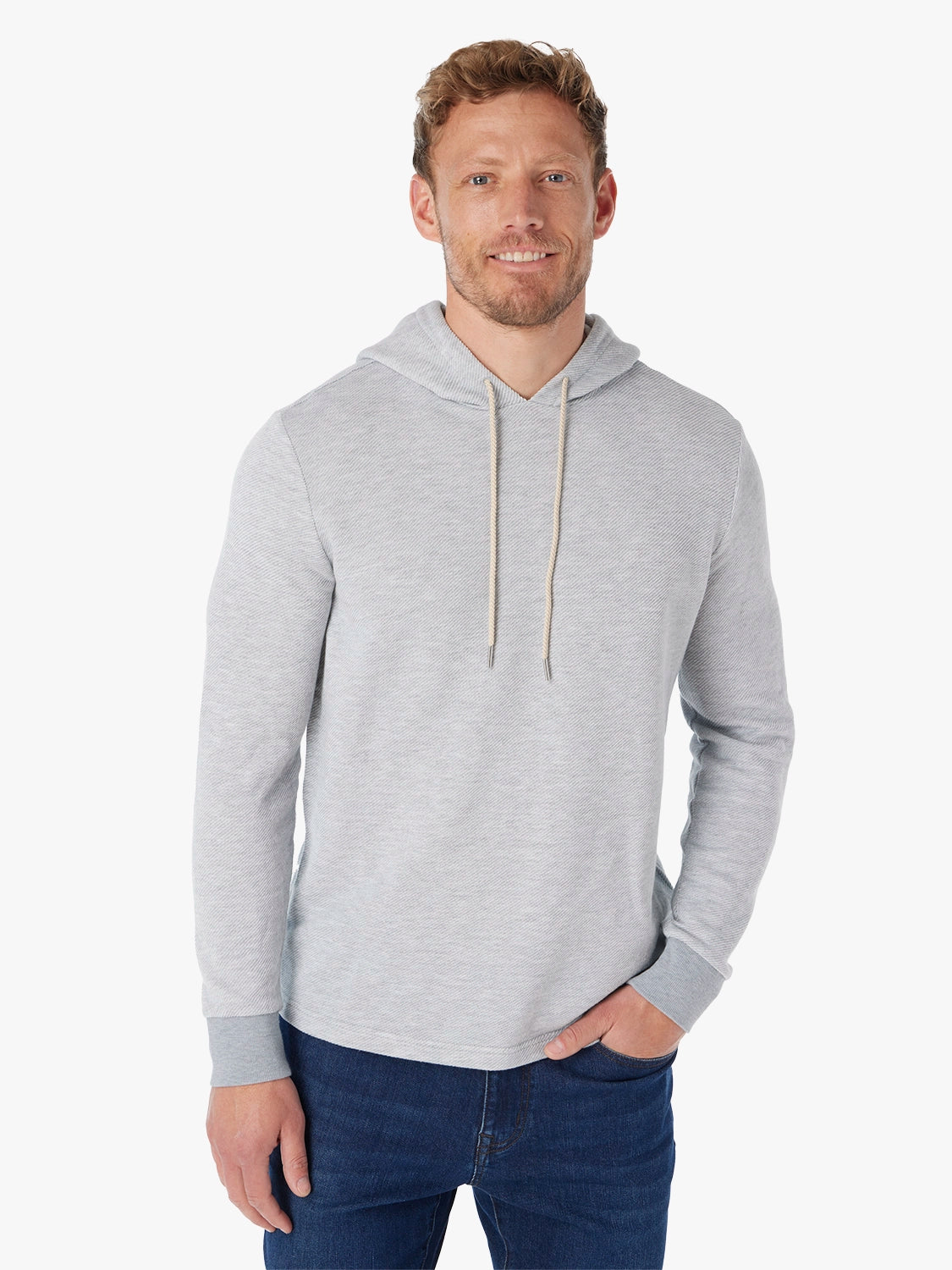 Man wearing a gray tailwind hoodie and blue jeans on a white background