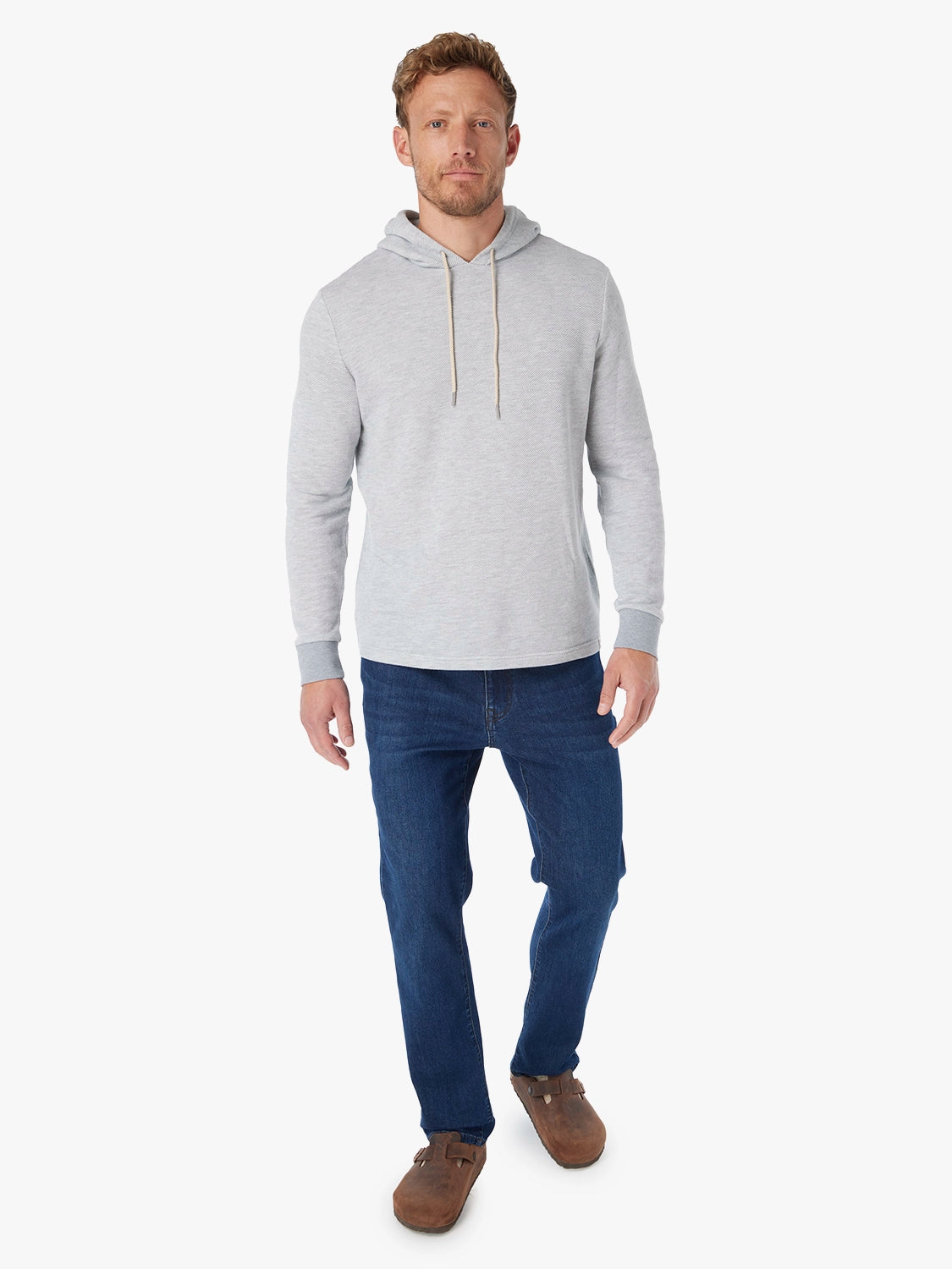 Man wearing a grey tailwind hoodie and blue jeans on a white background