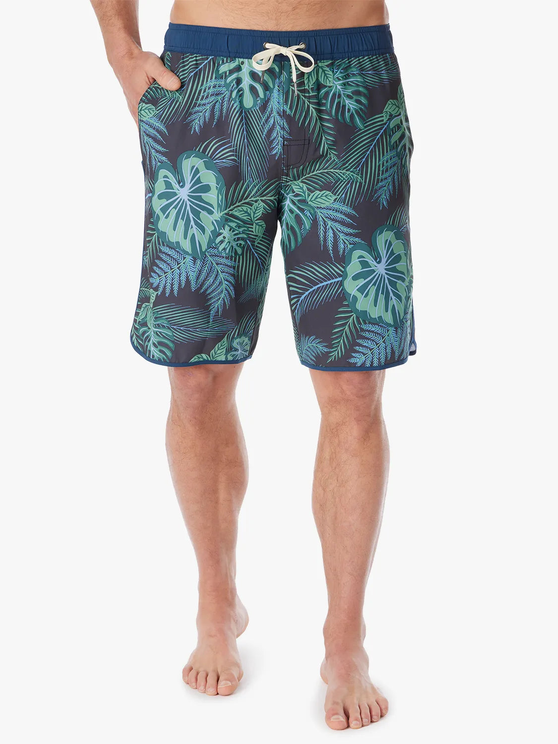 A person wearing a pair of Anchor Trunks in 10 inch inseam with a navy blue and green leaf pattern, featuring a drawstring waist on a white background. 