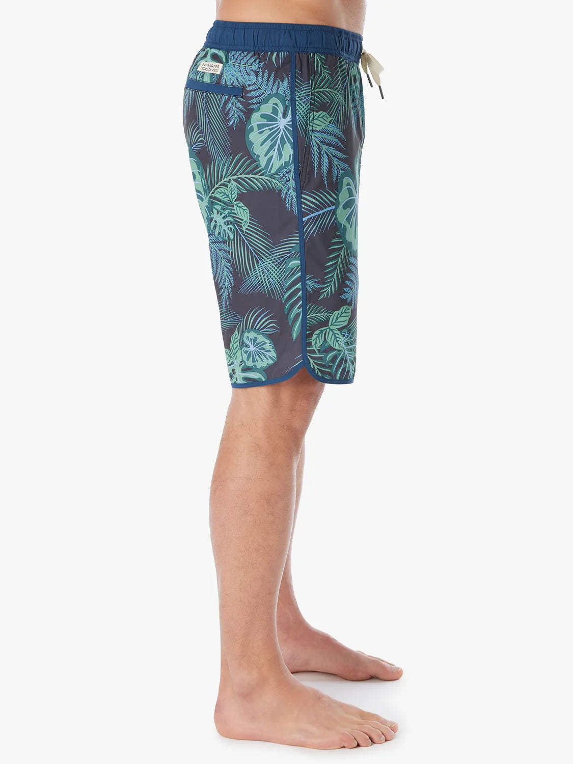 A person wearing a pair of Anchor Trunks in 10 inch inseam with a navy blue and green leaf pattern, showing a side view on a white background. 