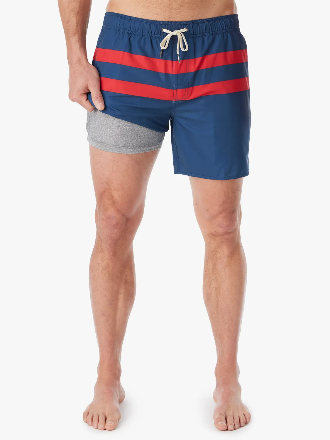 A person wearing a pair of 6 inch navy anchor trunk shorts with two red horizontal stripes and a drawstring waist, showing the liner with a white background. 