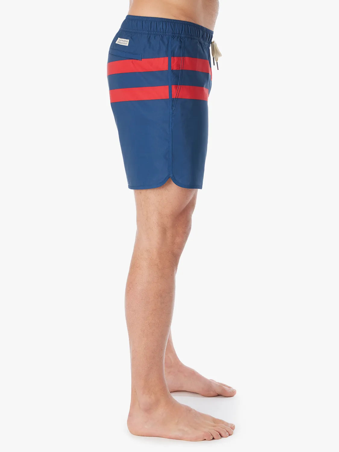 A person wearing a pair of 6 inch navy anchor trunk shorts with two red horizontal stripes and a drawstring waist, showing the side view with a white background. 
