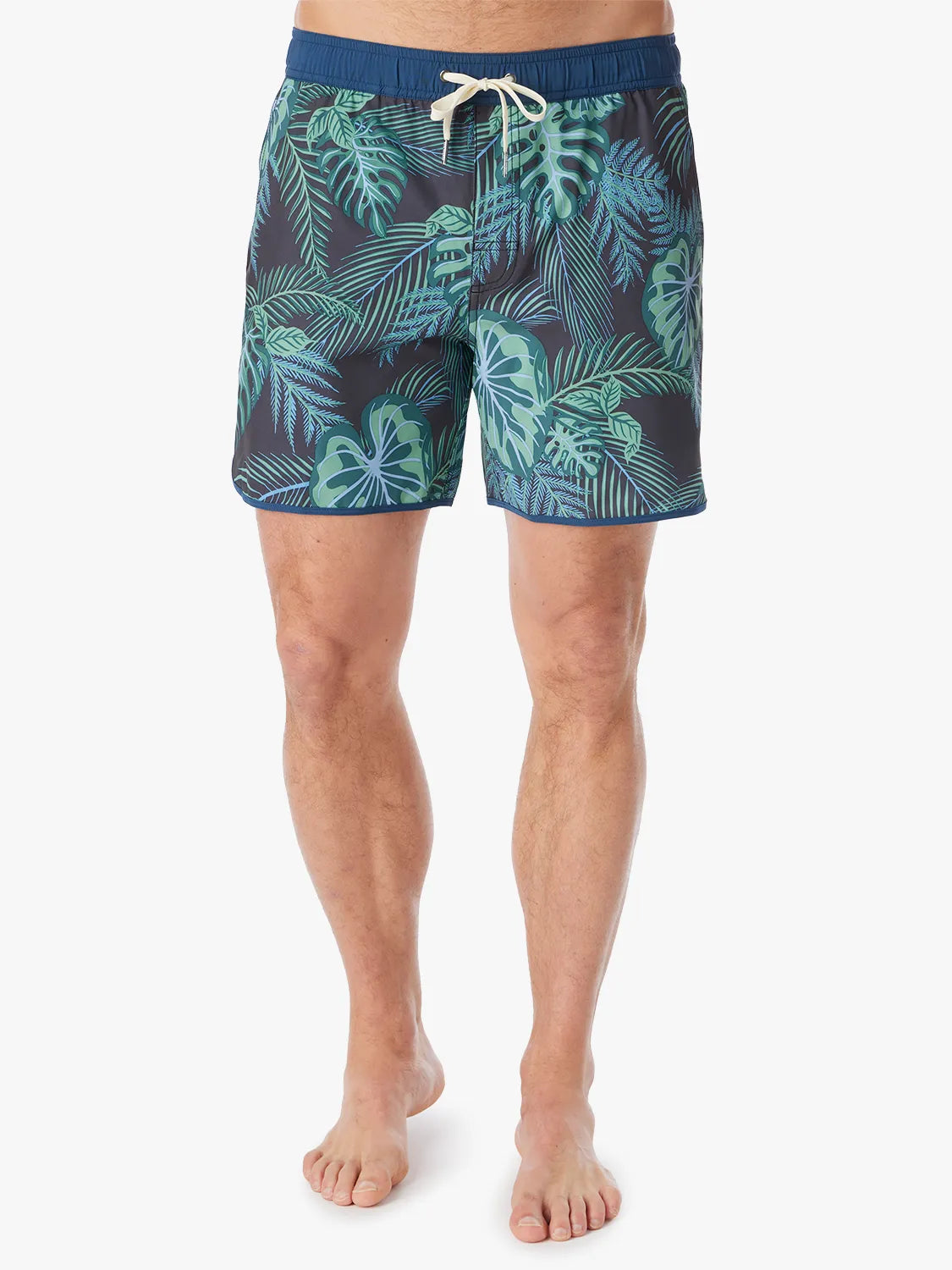 A person wearing a pair of Anchor Trunks in 6 inch inseam with a navy blue and green leaf pattern, featuring a drawstring waist on a white background. 
