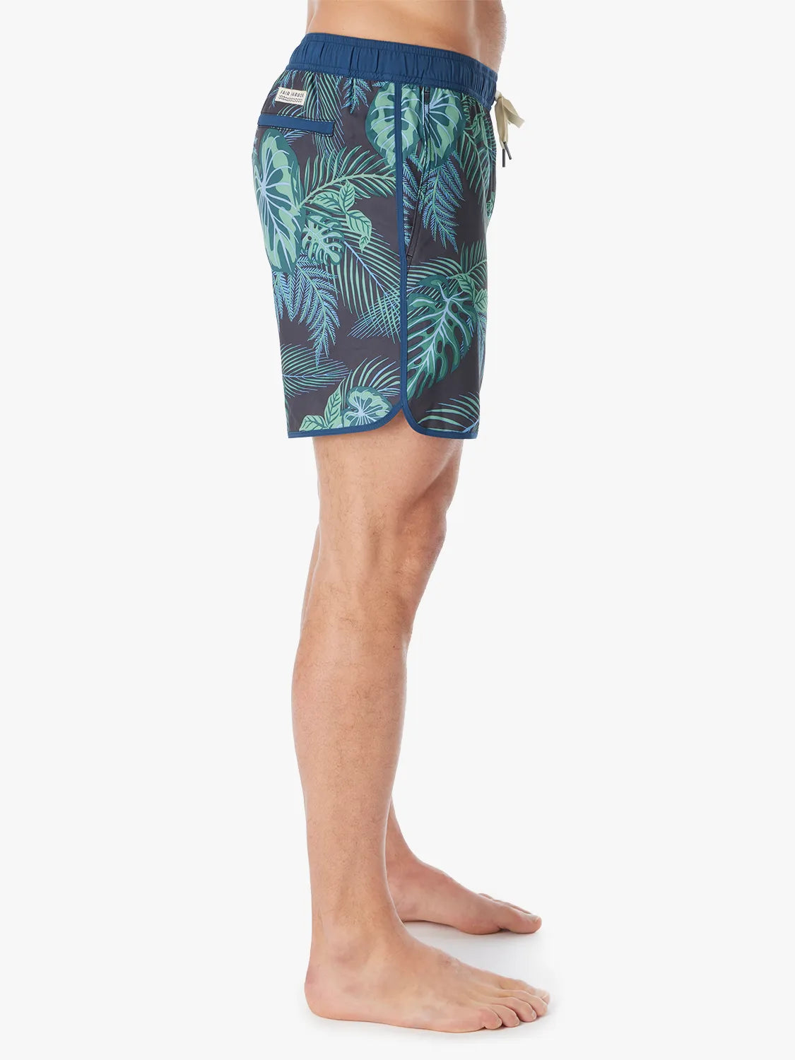A person wearing a pair of Anchor Trunks in 6 inch inseam with a navy blue and green leaf pattern, showing a side view on a white background. 