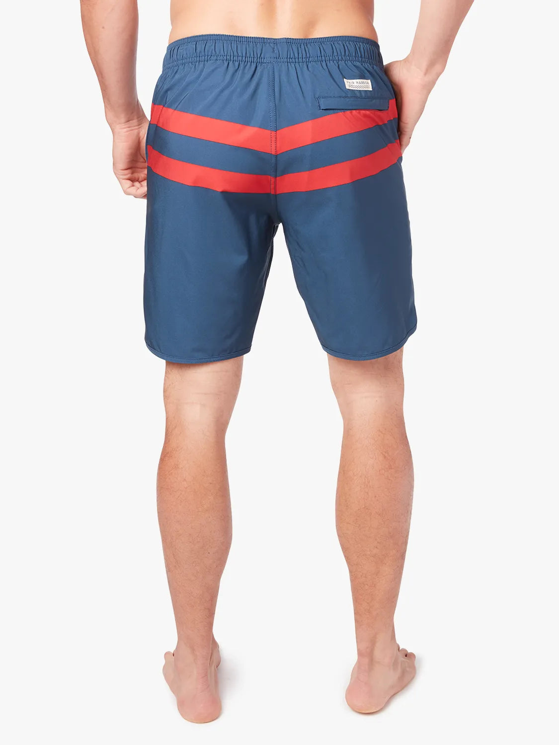 A person wearing a pair of 8 inch navy anchor trunk shorts with two red horizontal stripes, showing the back view with a white background. 