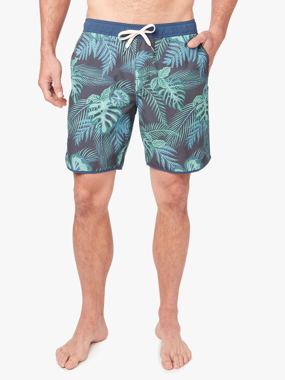 A person wearing a pair of Anchor Trunks in 8 inch inseam with a navy blue and green leaf pattern, featuring a drawstring waist on a white background. 