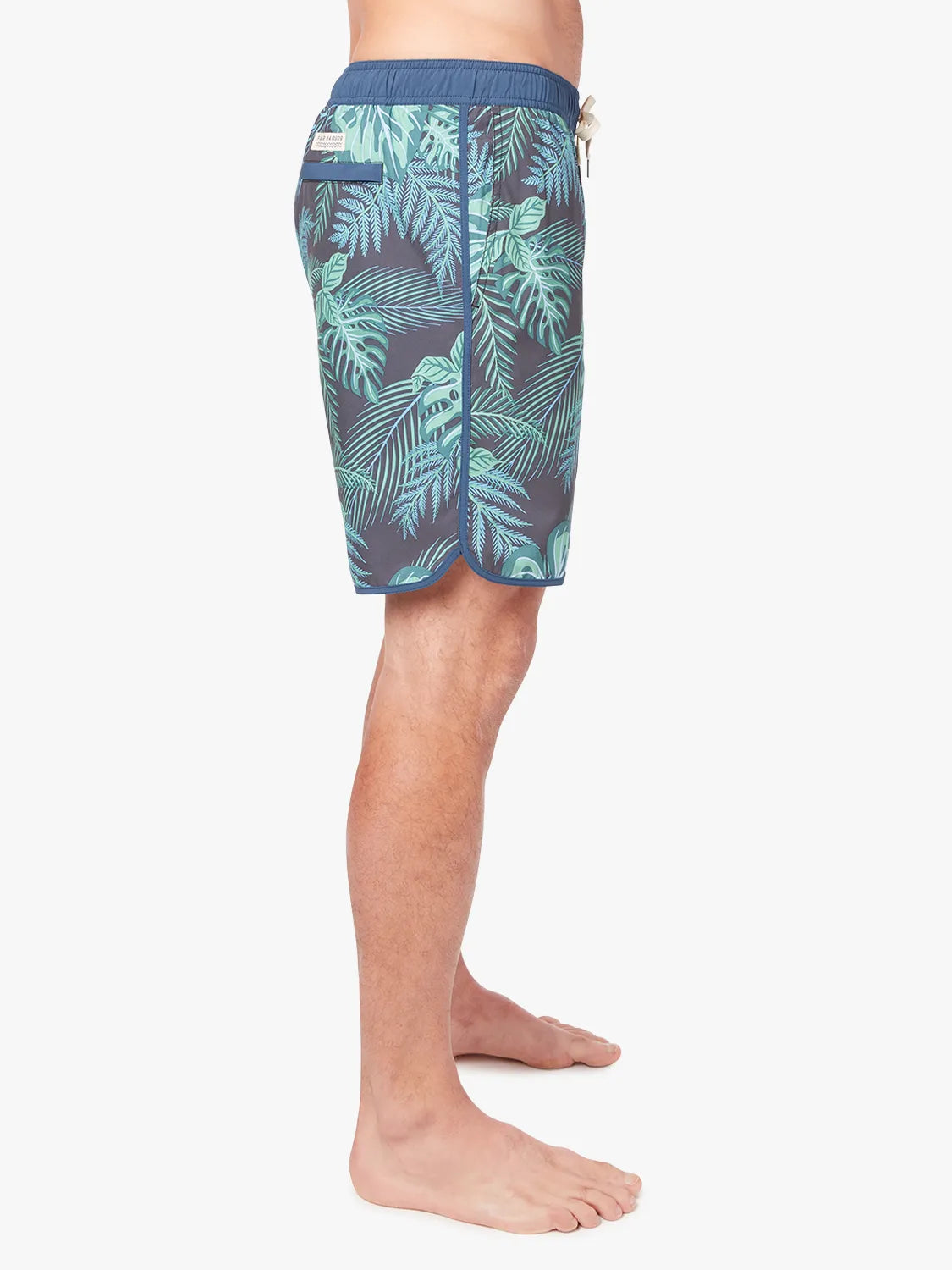 A person wearing a pair of Anchor Trunks in 8 inch inseam with a navy blue and green leaf pattern, showing a side view on a white background. 