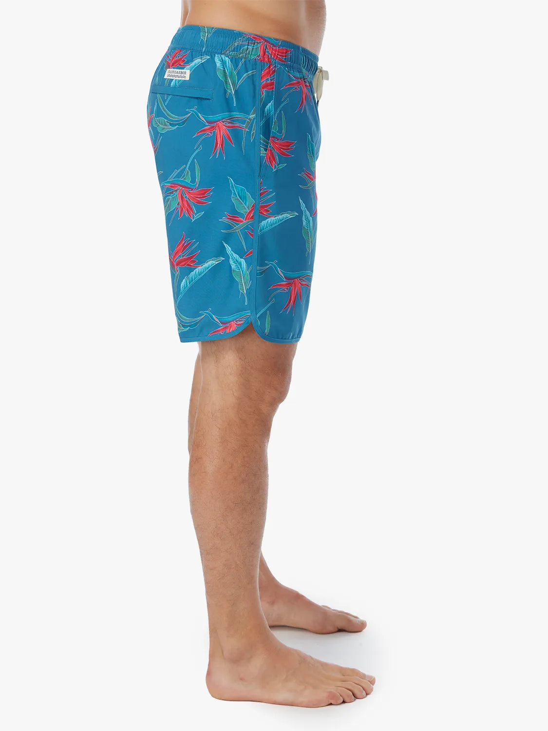 A person wearing a pair of teal blue Anchor Trunk with a red and green bird of paradise print, showing the side view on a white background. 
