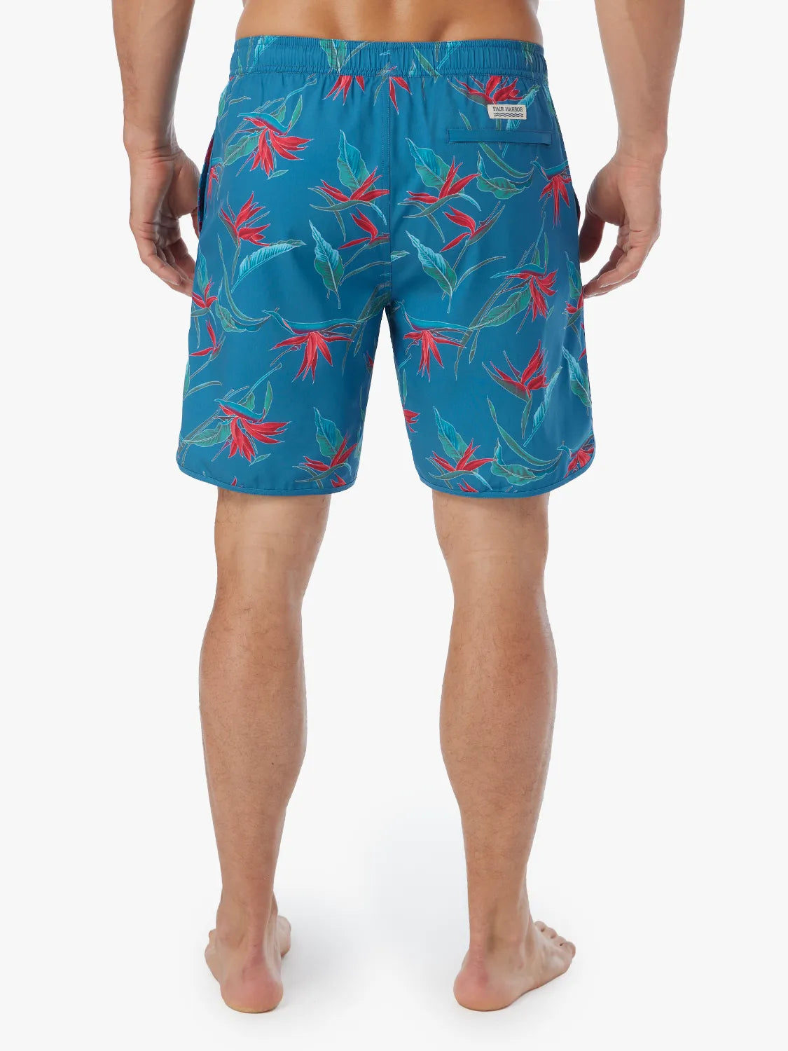 A person wearing a pair of teal blue Anchor Trunk with a red and green bird of paradise print, showing the back view on a white background. 