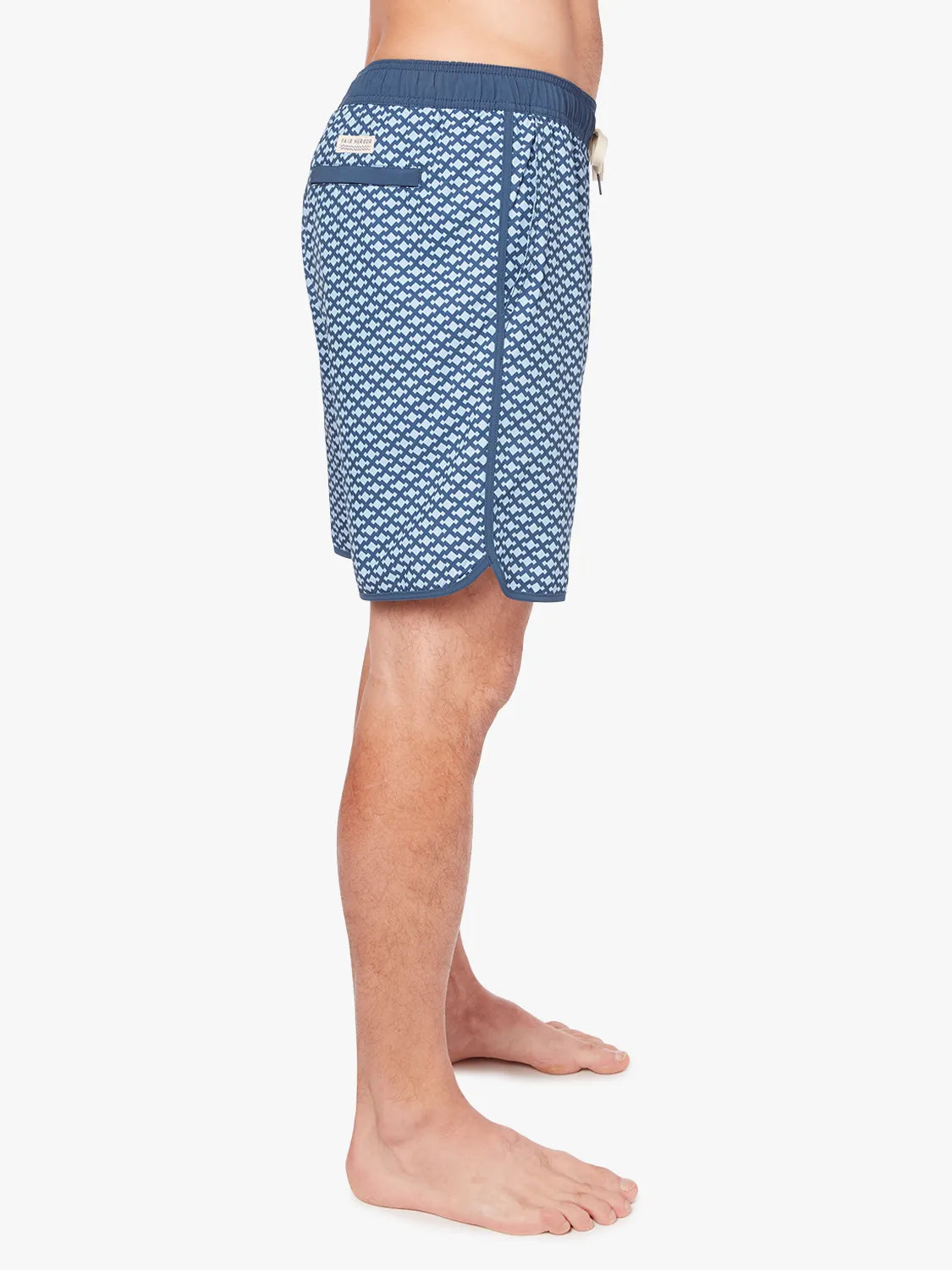 A person wearing a pair of Anchor Trunk in 8 inch inseam with a geometric pattern in shades of blue, featuring a drawstring waist showing the side view against a white background. 