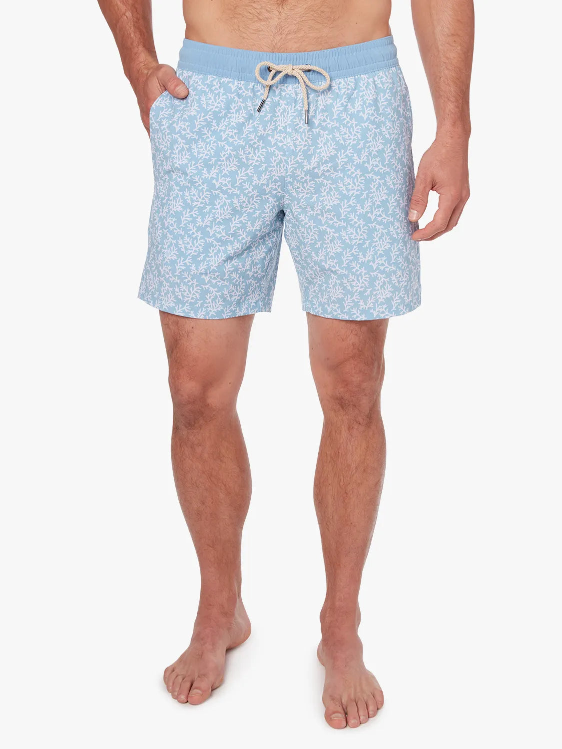 Person wearing a pair of mens Bayberry swim trunks with a floral mist seaweed pattern, light blue in color, with a drawstring elastic waistband.