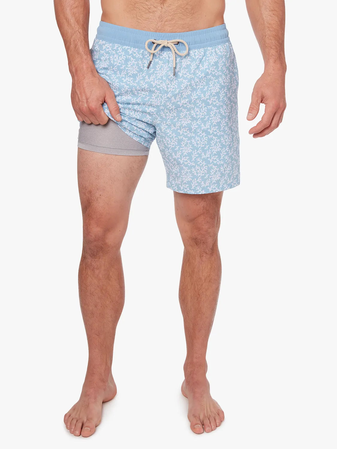 Person wearing a pair of mens Bayberry swim trunks with a floral mist seaweed pattern, light blue in color, with a drawstring elastic waistband - showing the liner. 