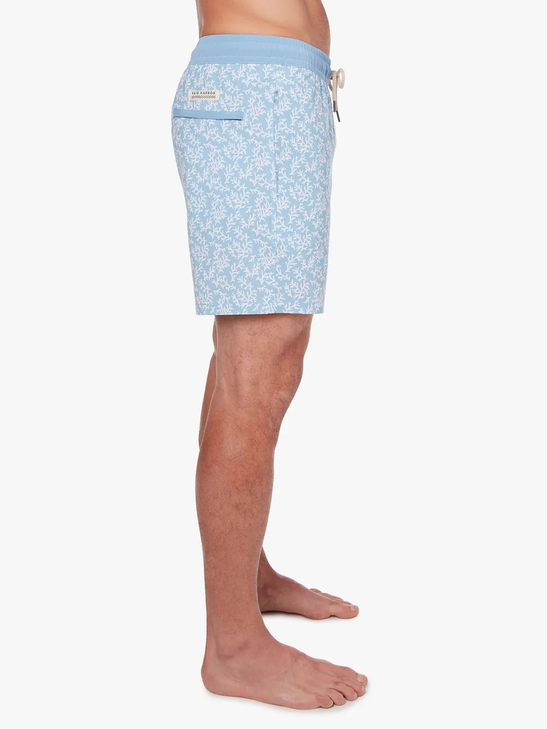 Person wearing a pair of mens Bayberry swim trunks with a floral mist seaweed pattern, light blue in color, with a drawstring elastic waistband. Showing the side view of shorts. 
