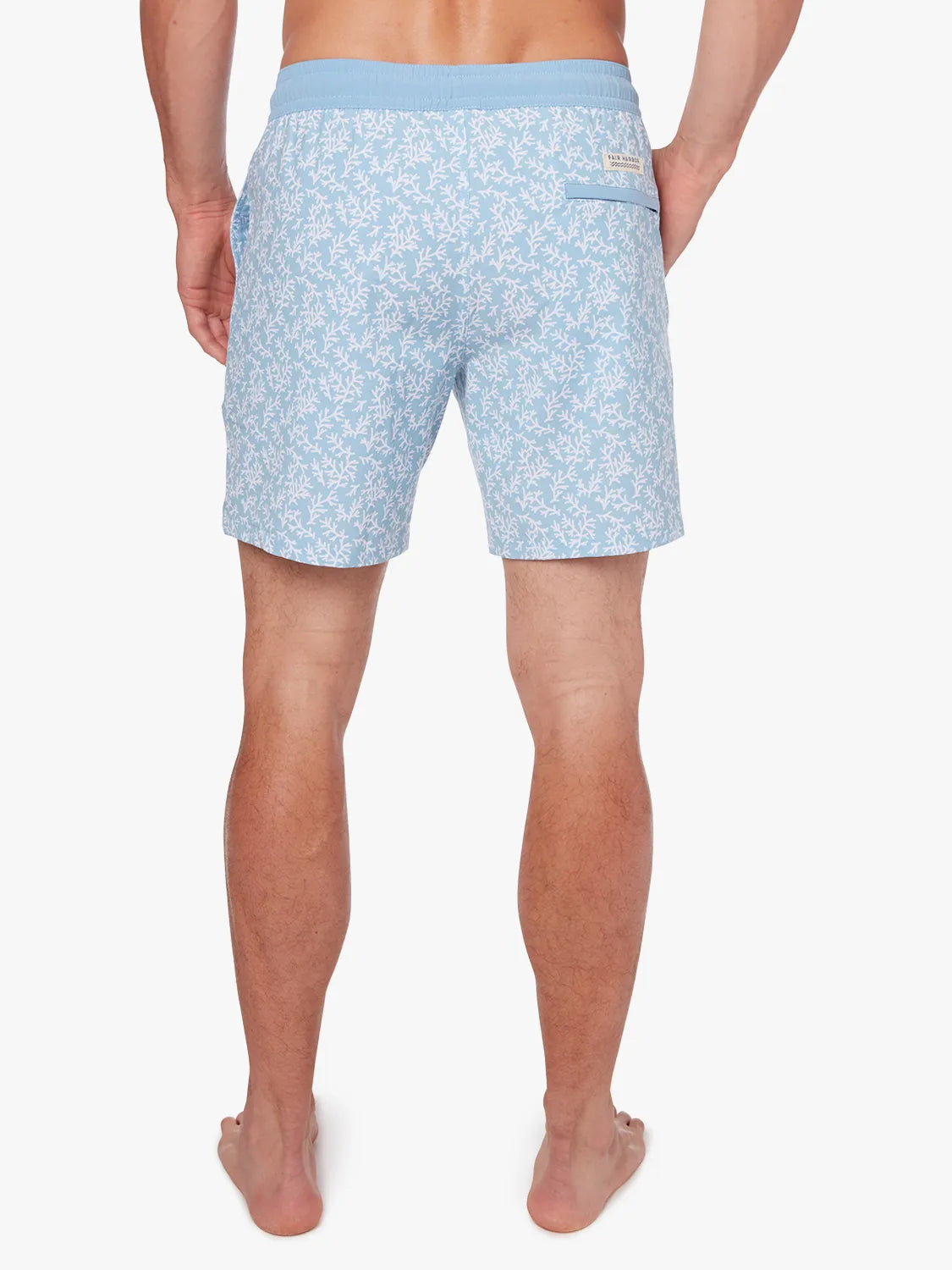 Person wearing a pair of mens Bayberry swim trunks with a floral mist seaweed pattern, light blue in color, with a drawstring elastic waistband. Showing the back view of shorts.
