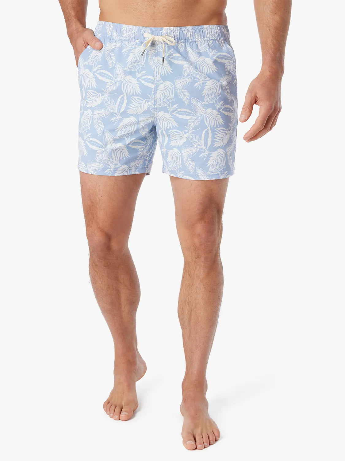 Person wearing light blue bungalow swim trunks with white tropical leaf pattern on a white background. 