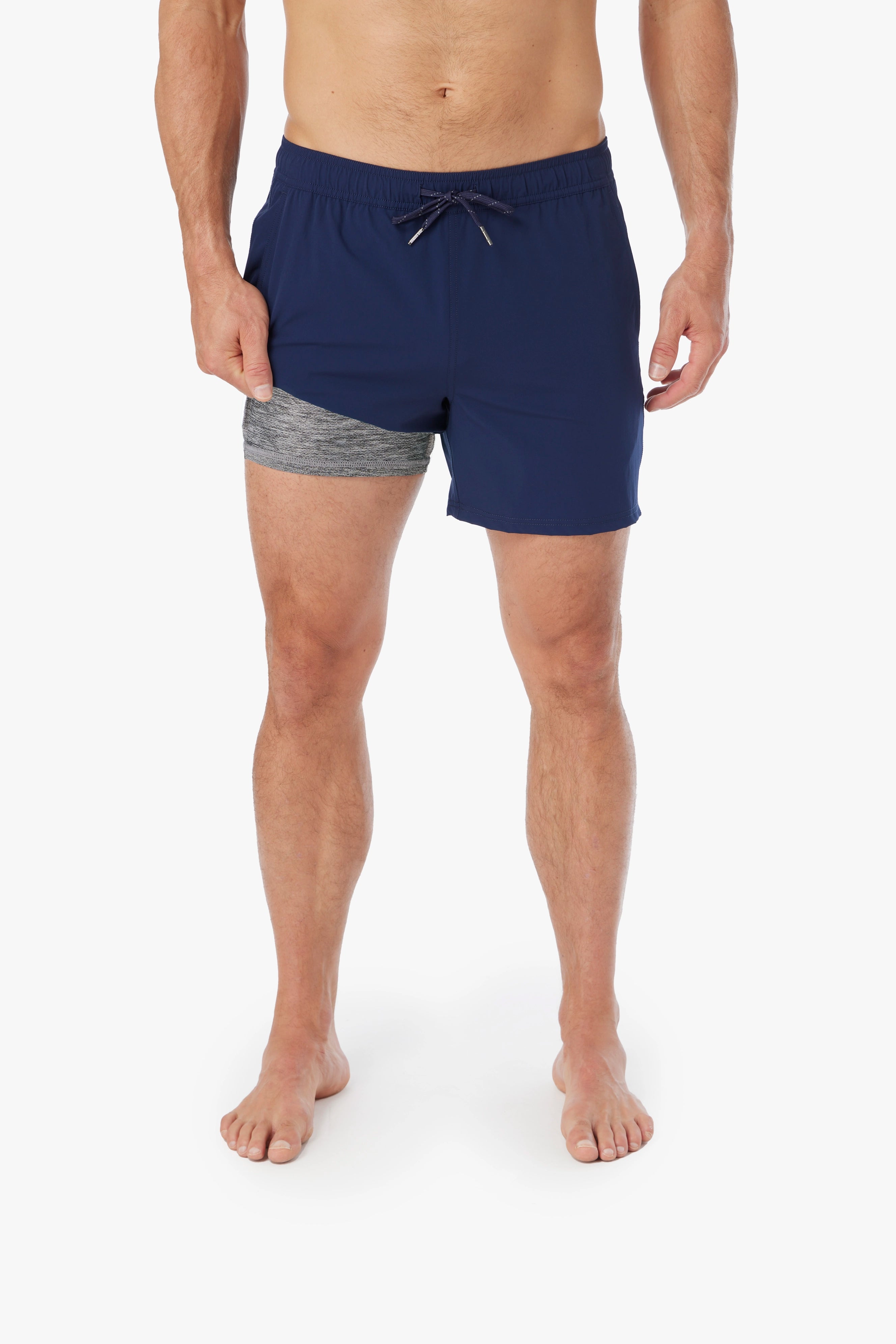 Person wearing pair of navy blue bungalow trunks with drawstring on a white background, showing the liner underneath. 