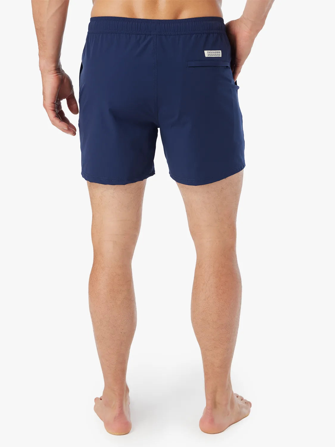 Person wearing pair of navy blue bungalow trunks with drawstring on a white background, showing the back view.