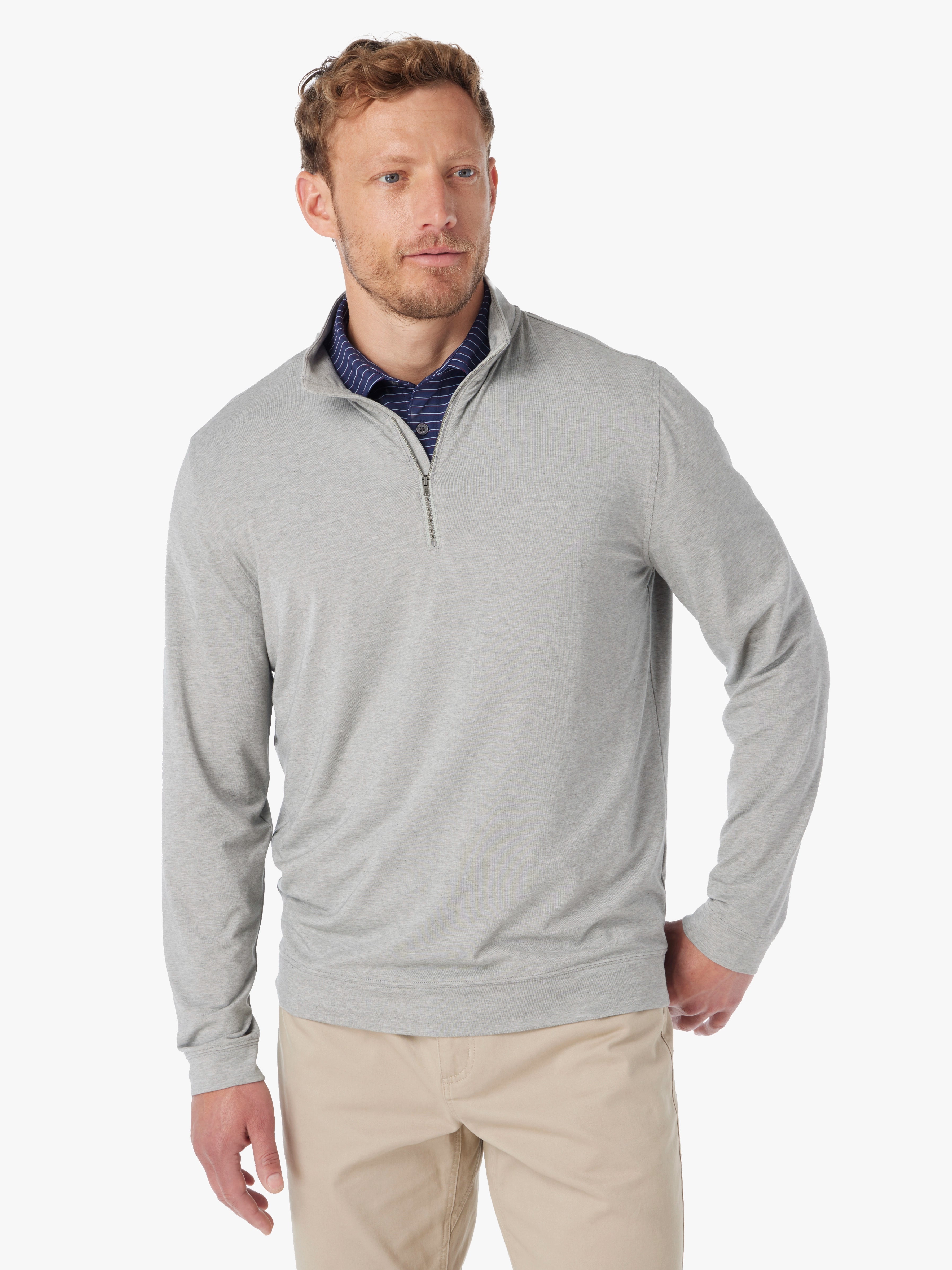 Man wearing heather grey compass pullover with a quarter zip on a white background, paired with compass polo underneath and khaki pants. 