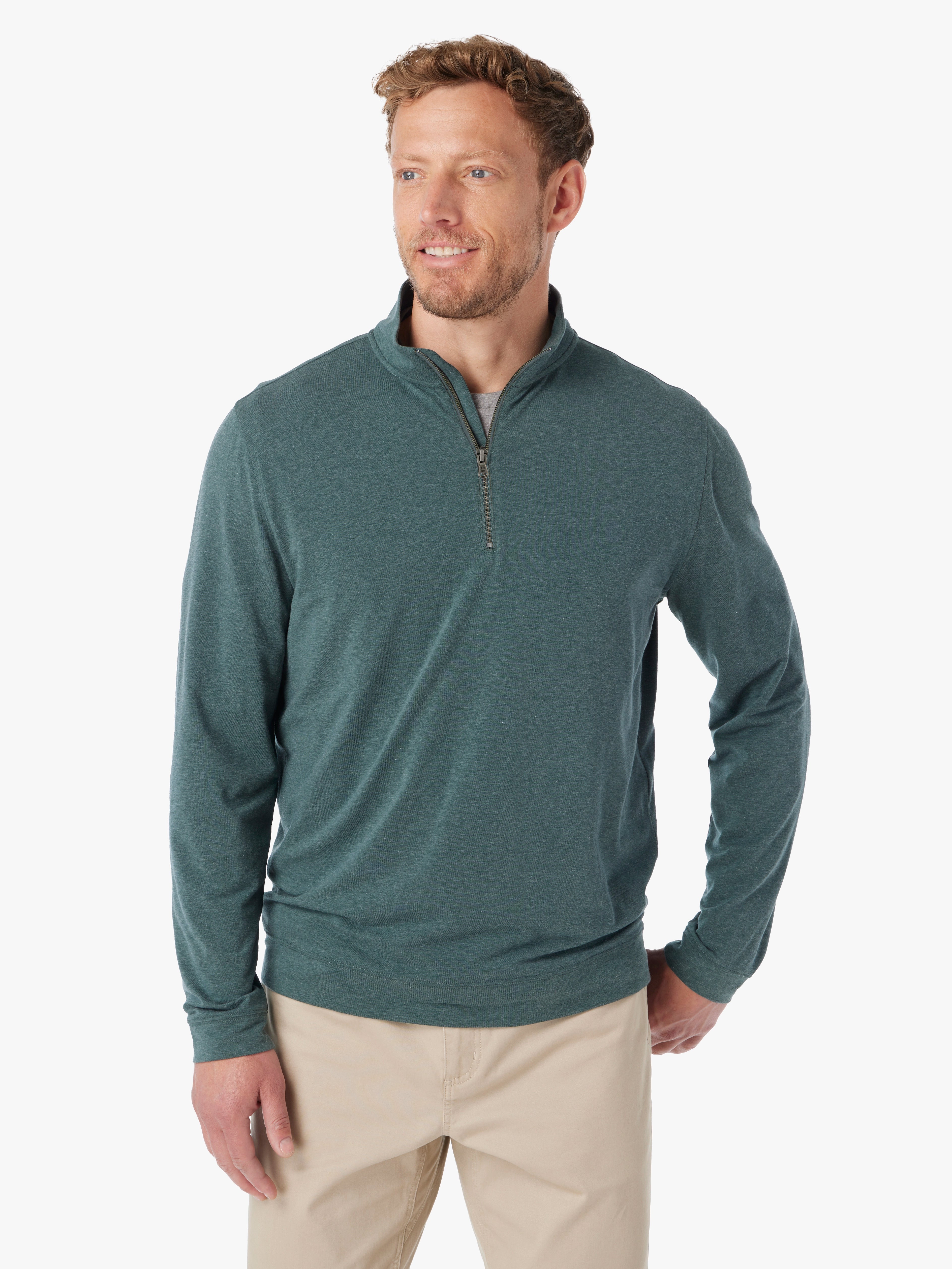 Man wearing olive green compass pullover with a quarter zip on a white background paired with khaki pants. 